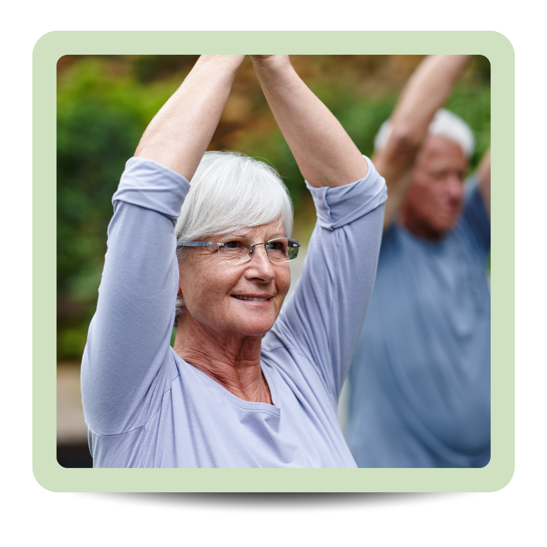 Older woman in blue shirt stretching with arms overhead outdoors, smiling, with a man also stretching in the background.
