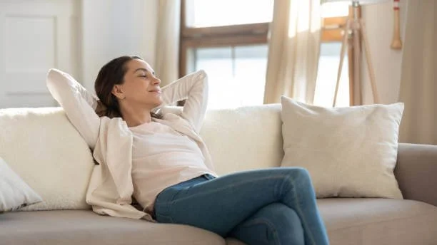Person relaxing on a sofa in a sunlit room.