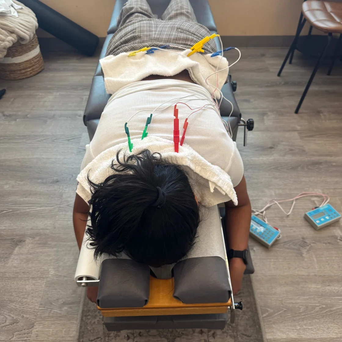 A person lying face down on a chiropractic or massage table with electrodes attached to their back.