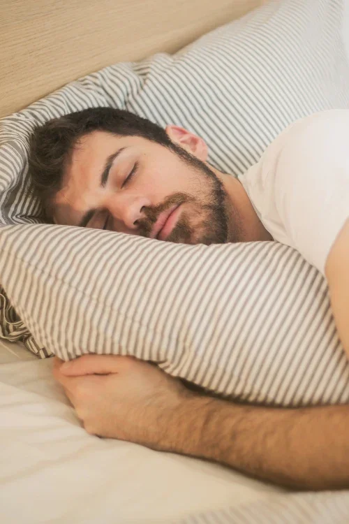 A man sleeping peacefully on a striped pillow with his arm resting on the bed.