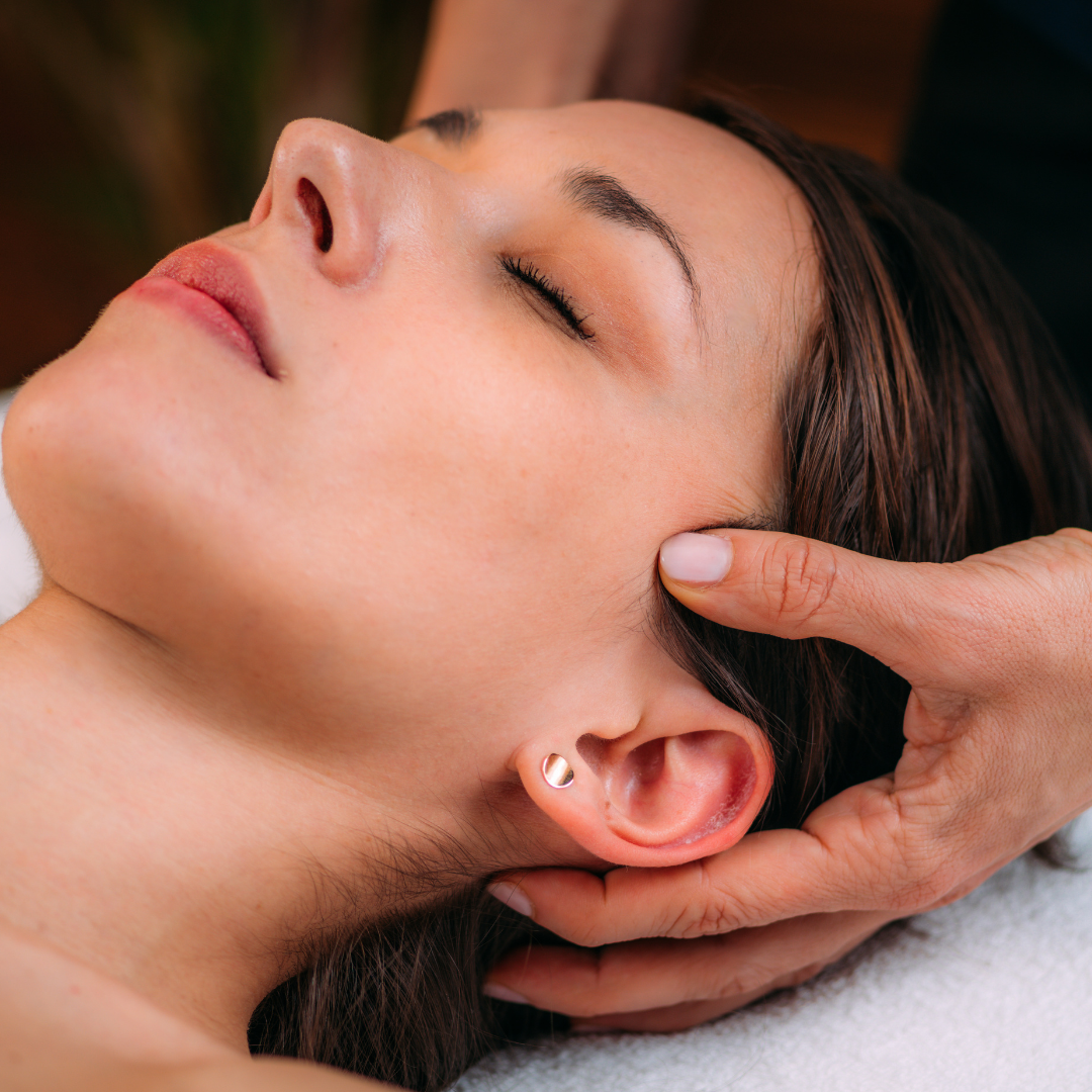 A woman receiving a relaxing head massage while lying down with her eyes closed.