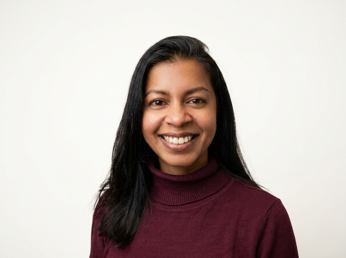 A woman with long black hair, smiling, wearing a maroon turtleneck sweater, standing in front of a plain white background.