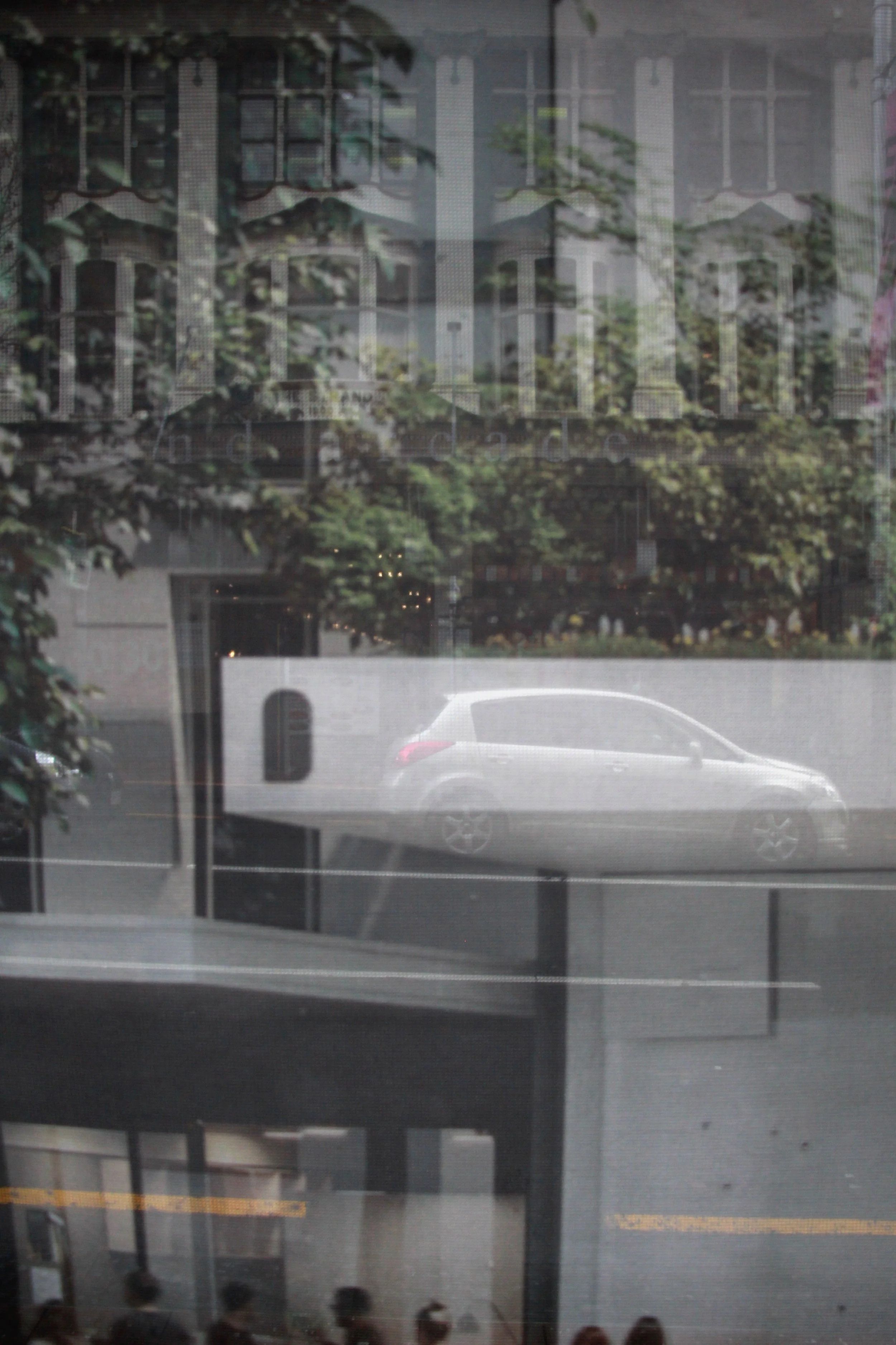 A printed see through graphic in the city, with cars and the street behind it, making for an abstract composition.