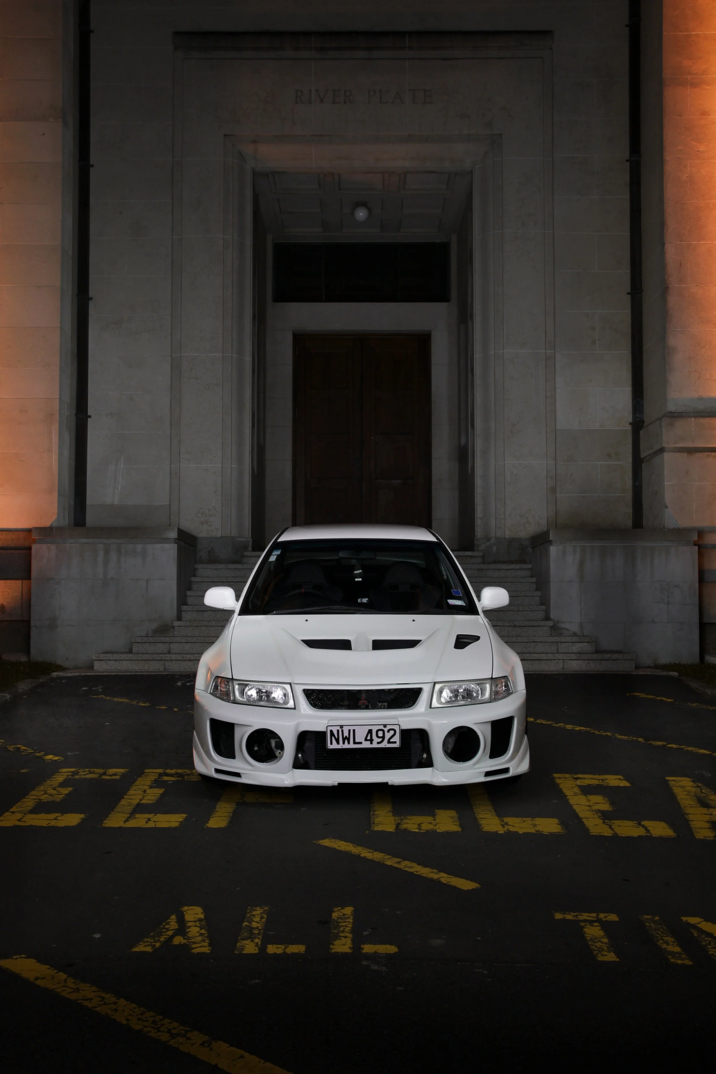 A white Mitsubishi Evo 5 parked in front of a building with a staircase.
