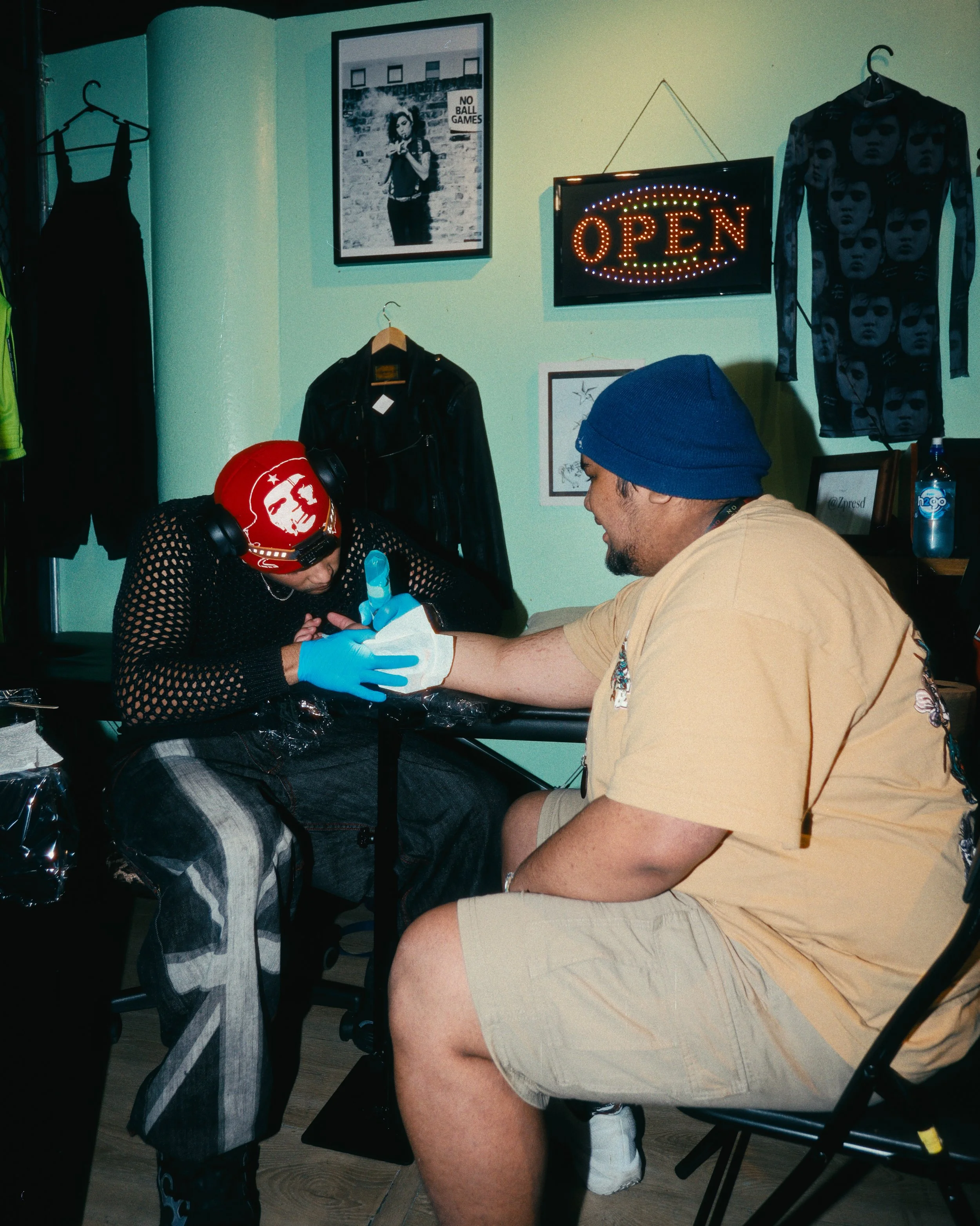 People getting a tattoo in a tattoo shop, with one person sitting and another person working on their arm.