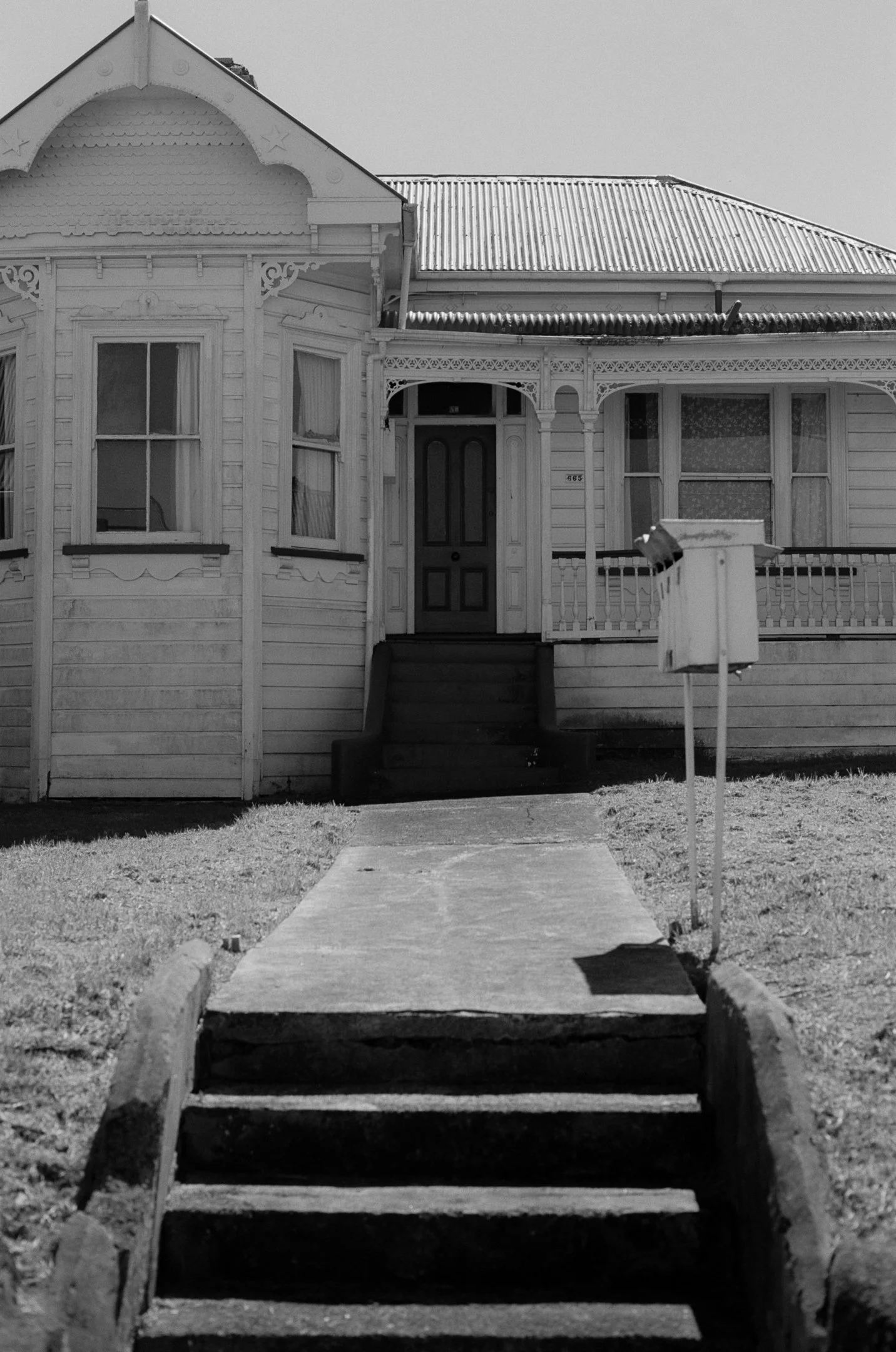 Black and white photo of a porch with steps leading up to the front door of an old house, featuring ornate trim and windows on either side of the door.
