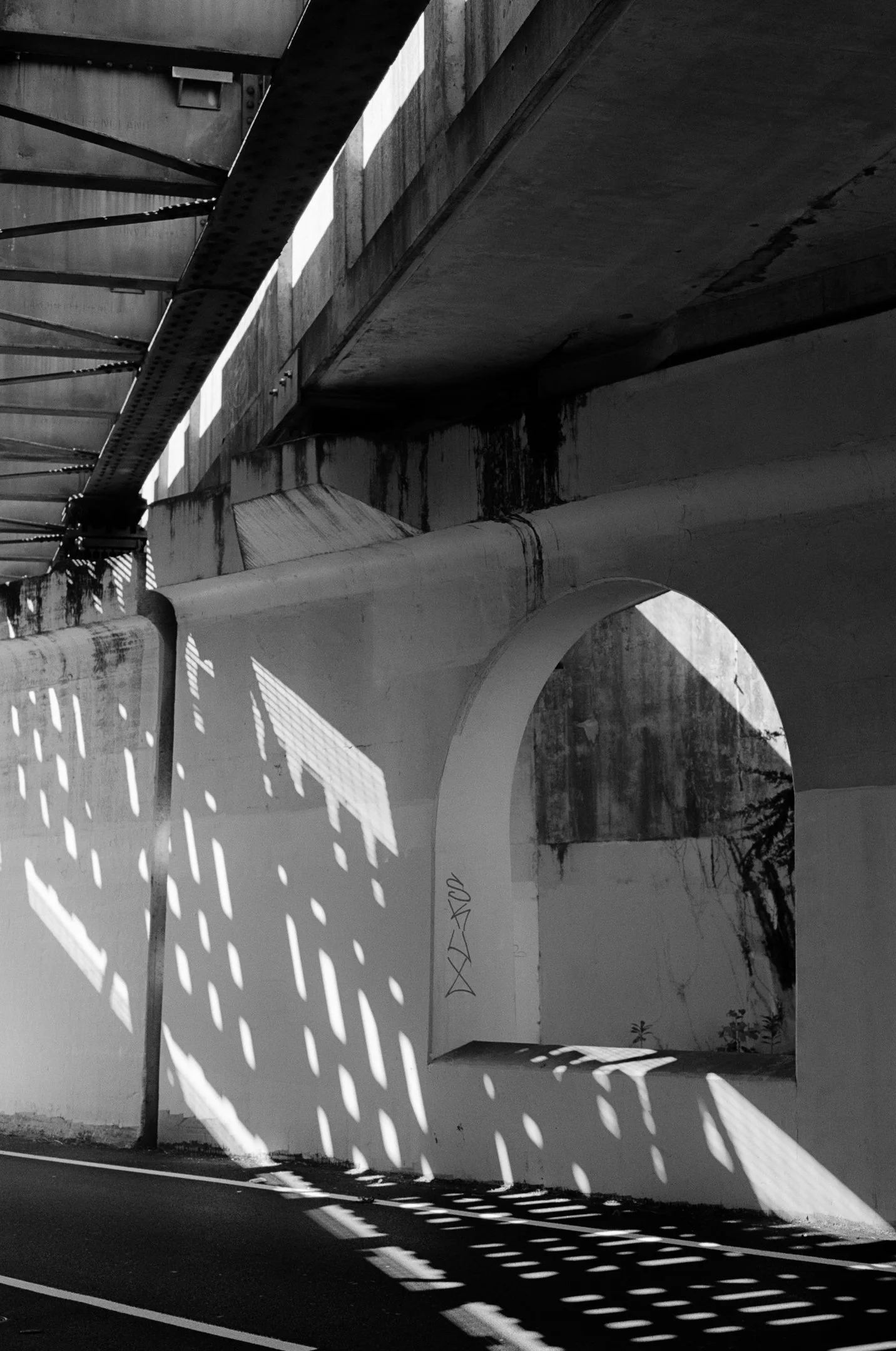 Black and white photo of patterned shadows on a concrete underpass and street, creating an abstract visual effect.