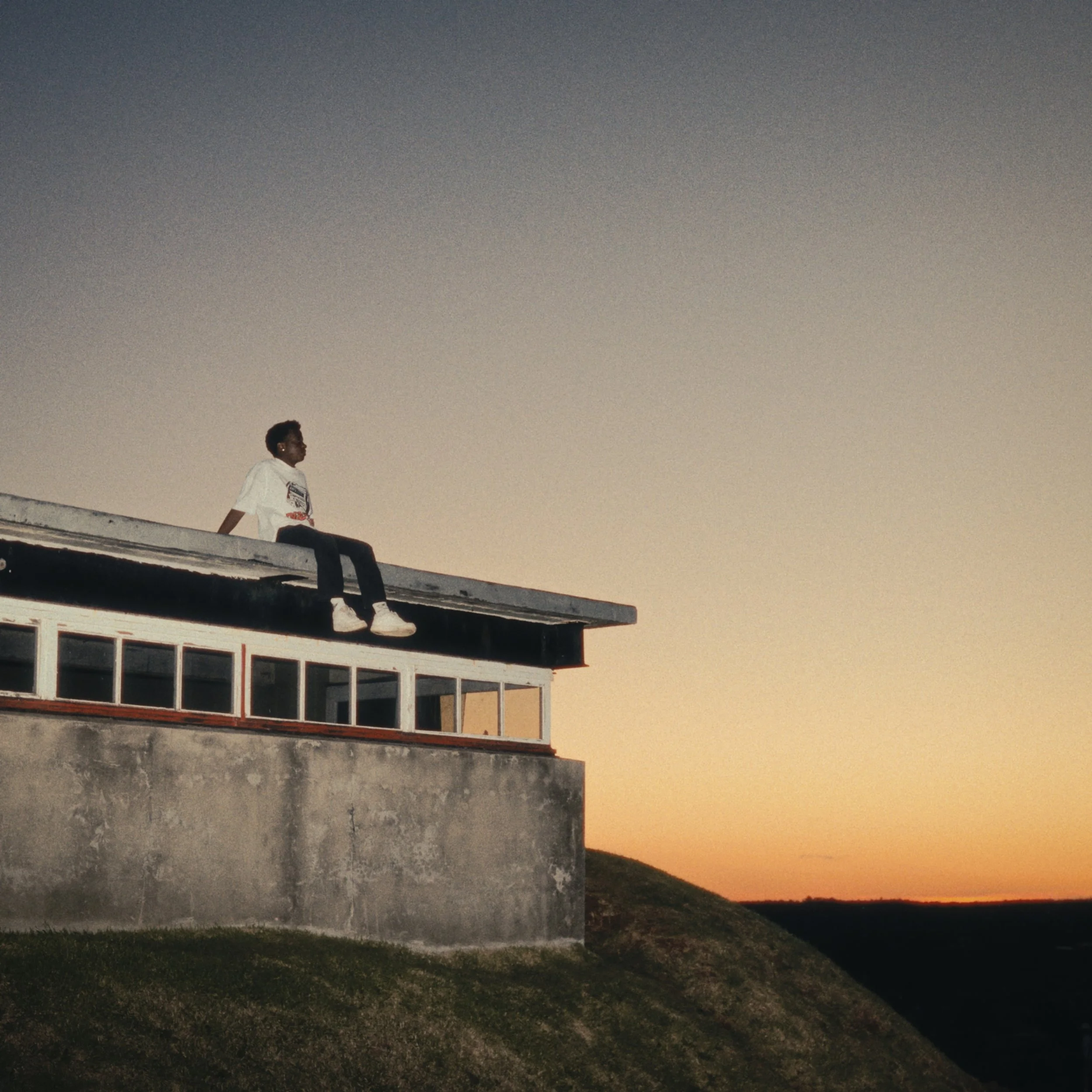 A person sitting on the edge of an old war building's roof during sunset.