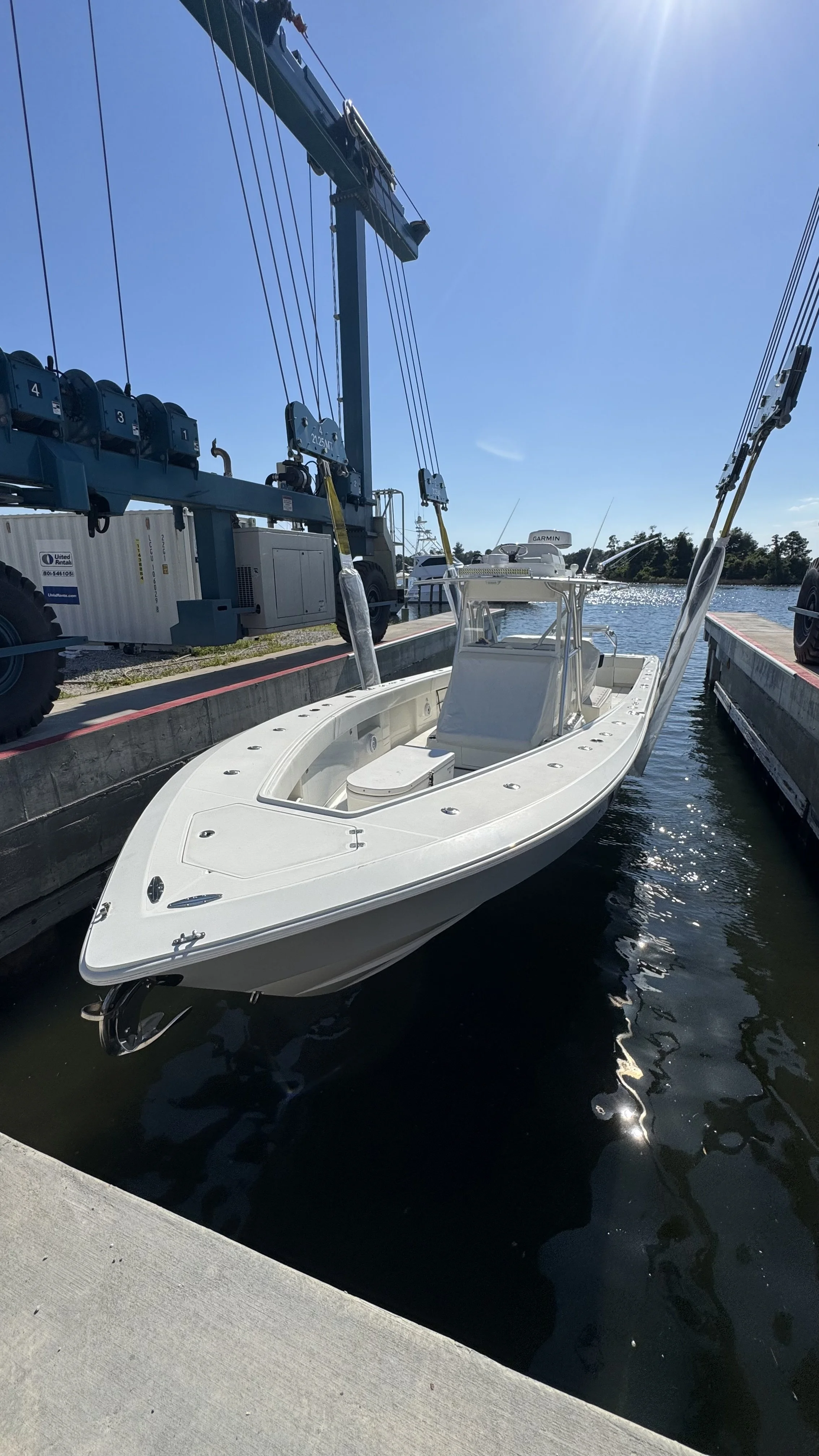 The front of a small boat taken from above as it is strapped to a marine travel lift and being lowered into the water.
