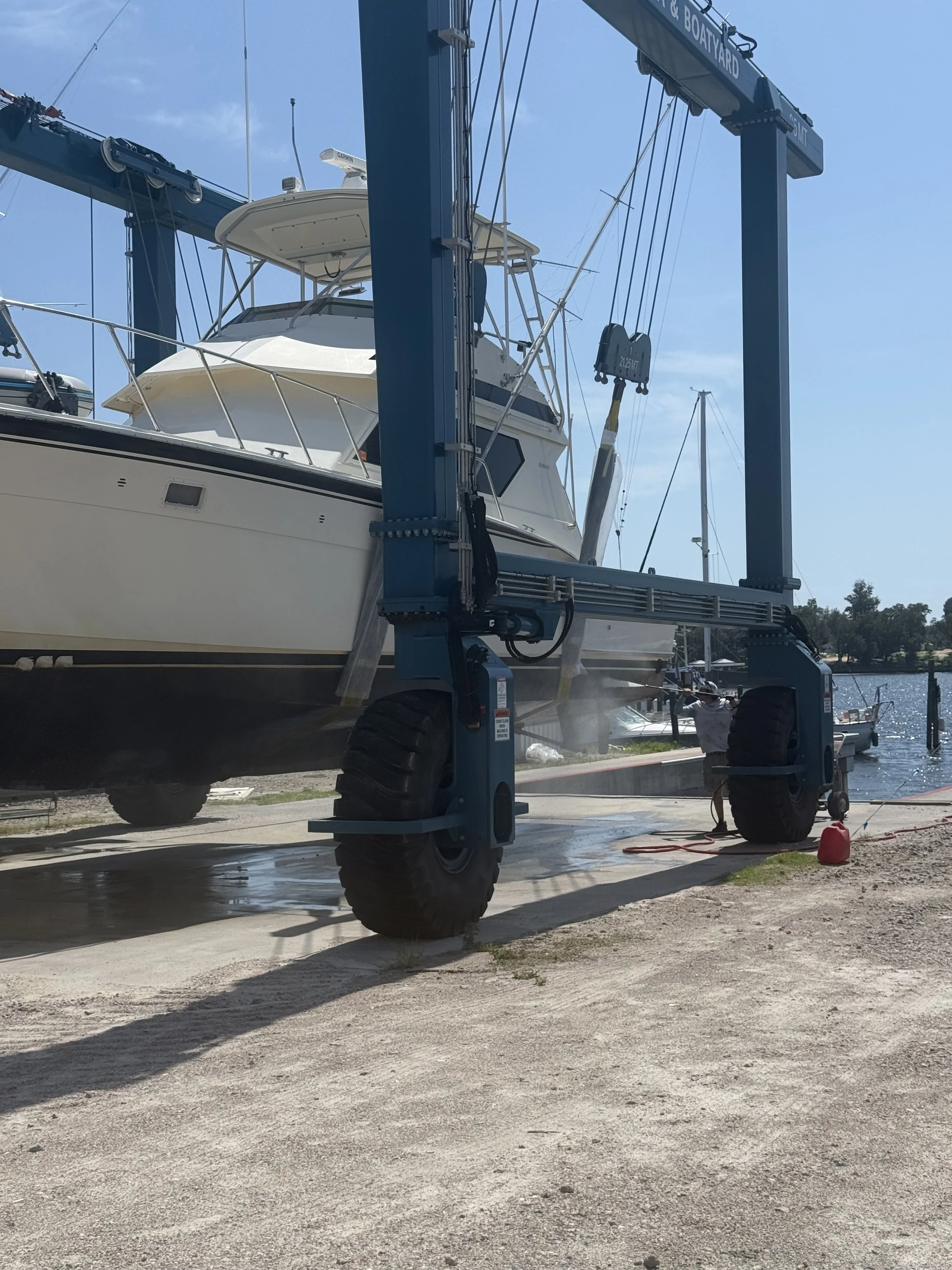 The front left hand side of a boat strapped into a marine travel lift over the ground about to move backward over the water.