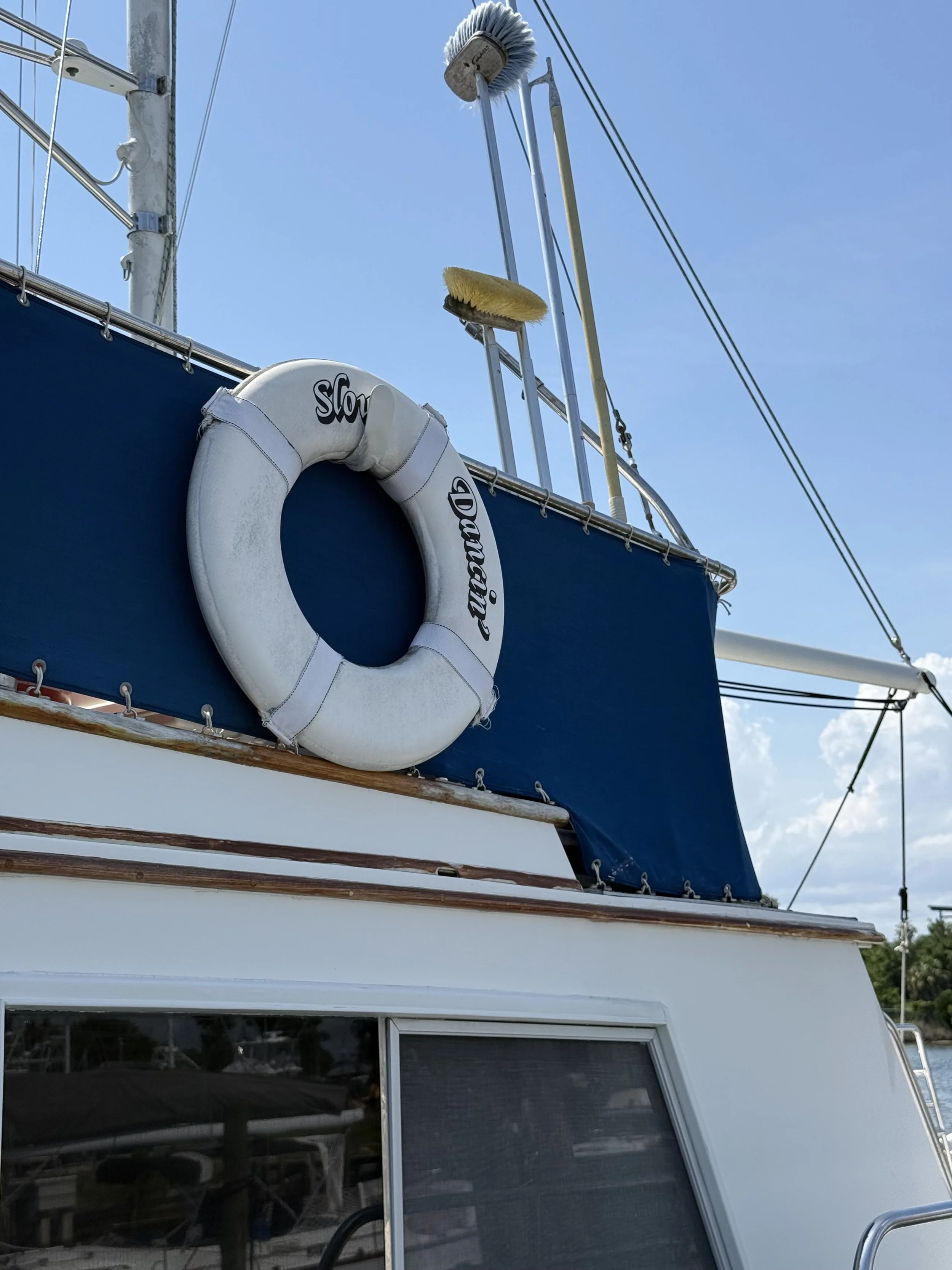 A close up picture of a part of the top of a boat with a life preserver ring with the boat name (Slow Dancin') printed on it and part of a blue sky with white clouds.