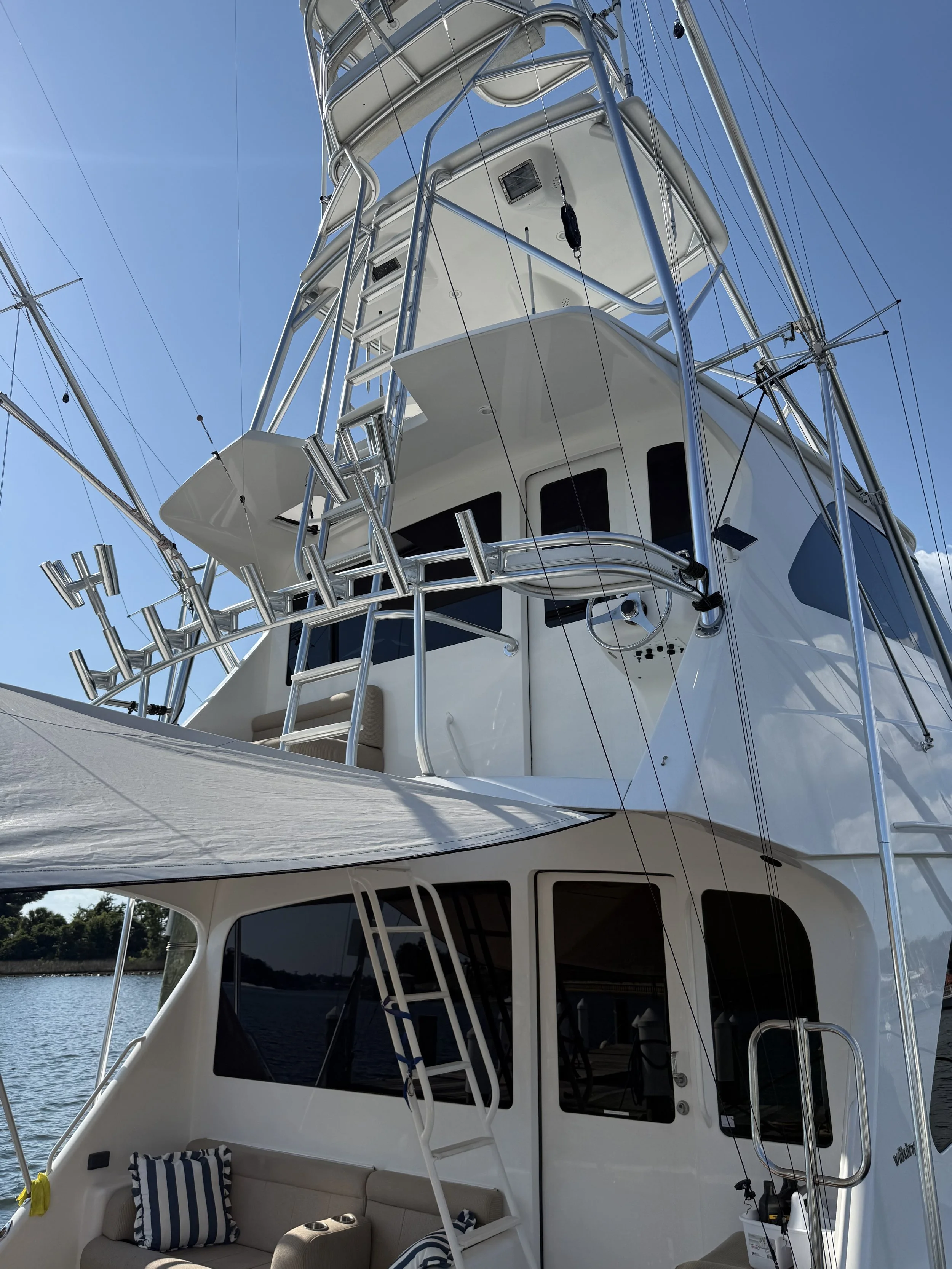 Upward view of a large white yacht docked at Panhandle Marina & Boatyard near a body of water, featuring multiple decks, a lounge area with striped pillows, and metal framework with equipment.