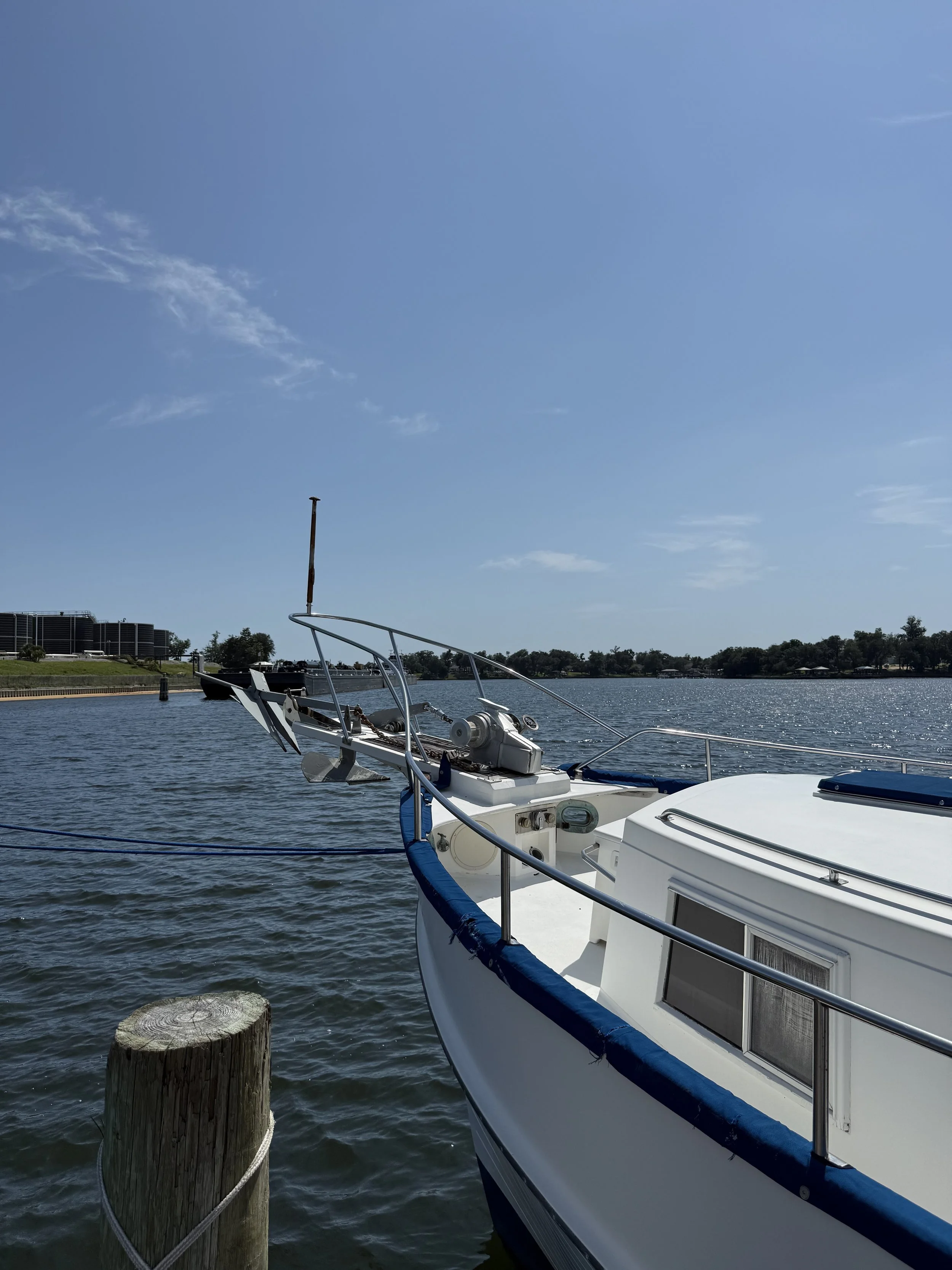 A picture taken at an angle of the left hand very front and tip of a boat with the water, sky, and treelike behind it.