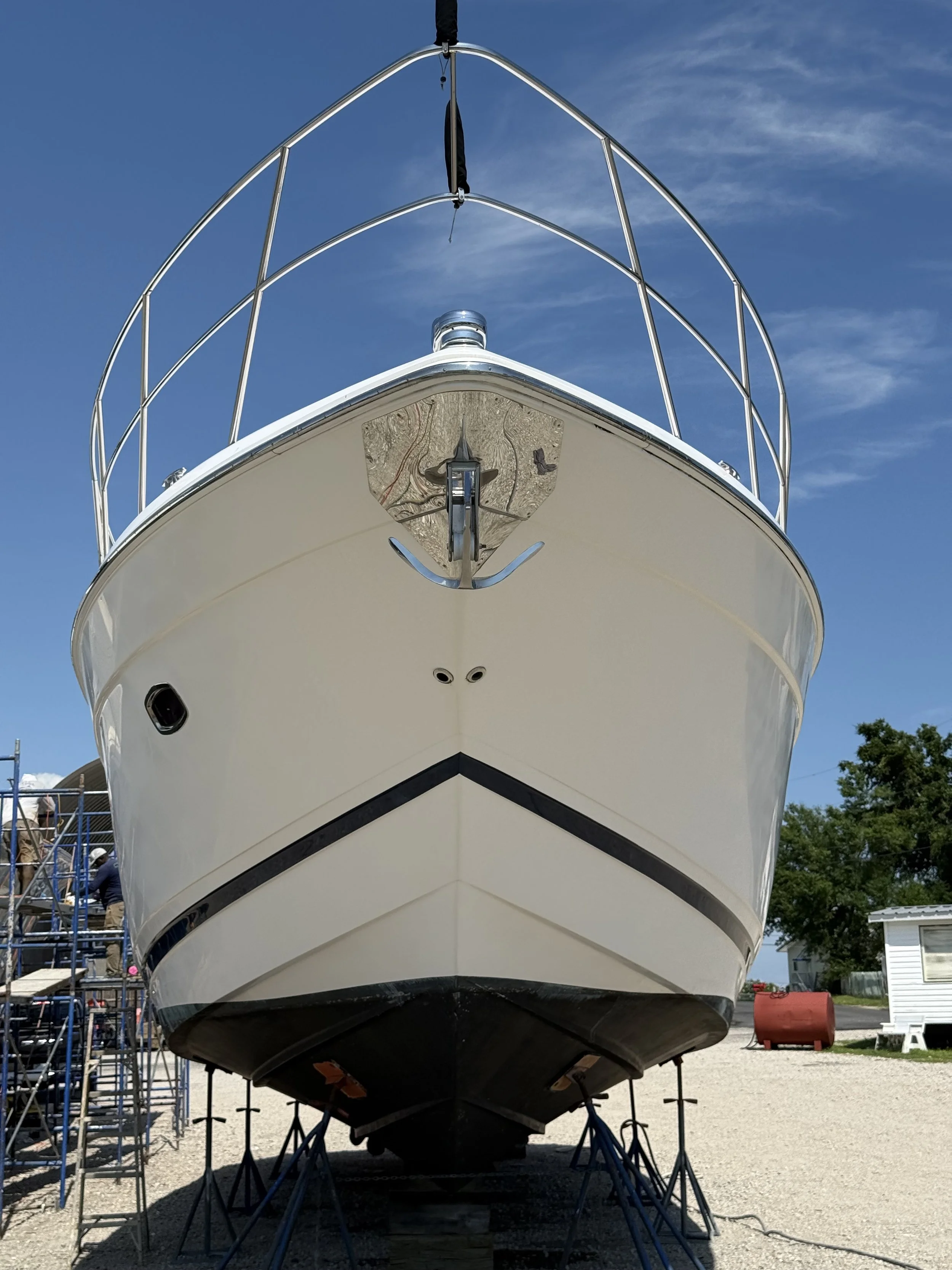 The front of a boat that is lifted from the ground for repairs and taken slightly under the boat so you can see the full size of the front of the boat.