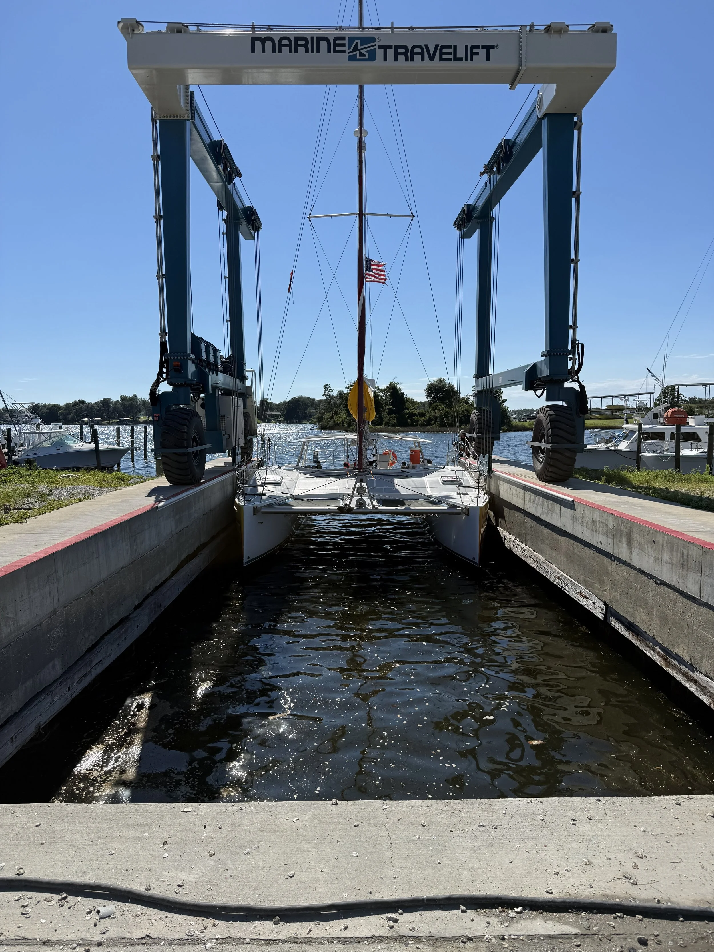 A big sailboat strapped in a marine travel lift being lowered into the water.