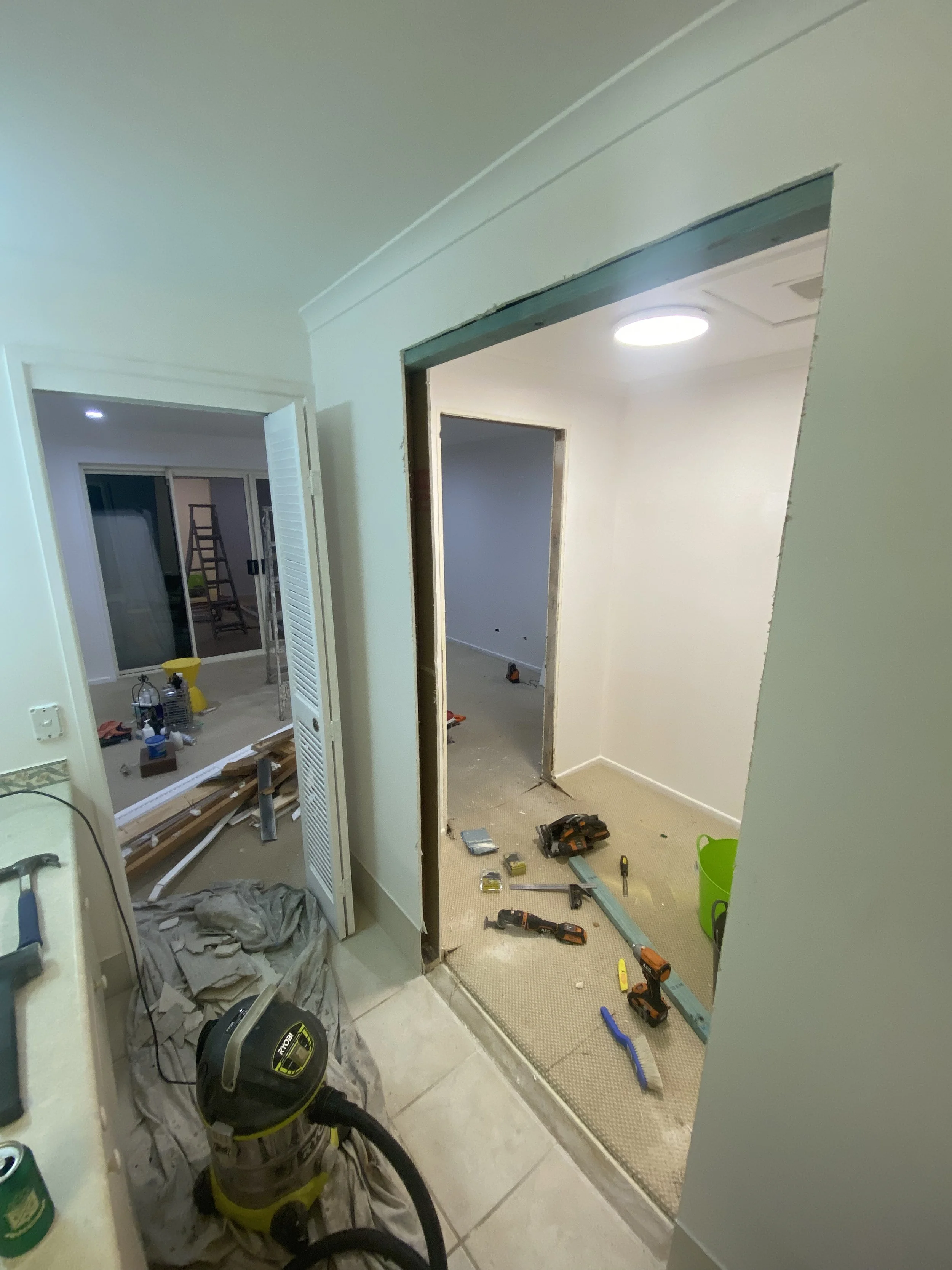 Interior of a room under renovation with tools and materials on the floor, doorways leading into other rooms, and drywall work in progress.