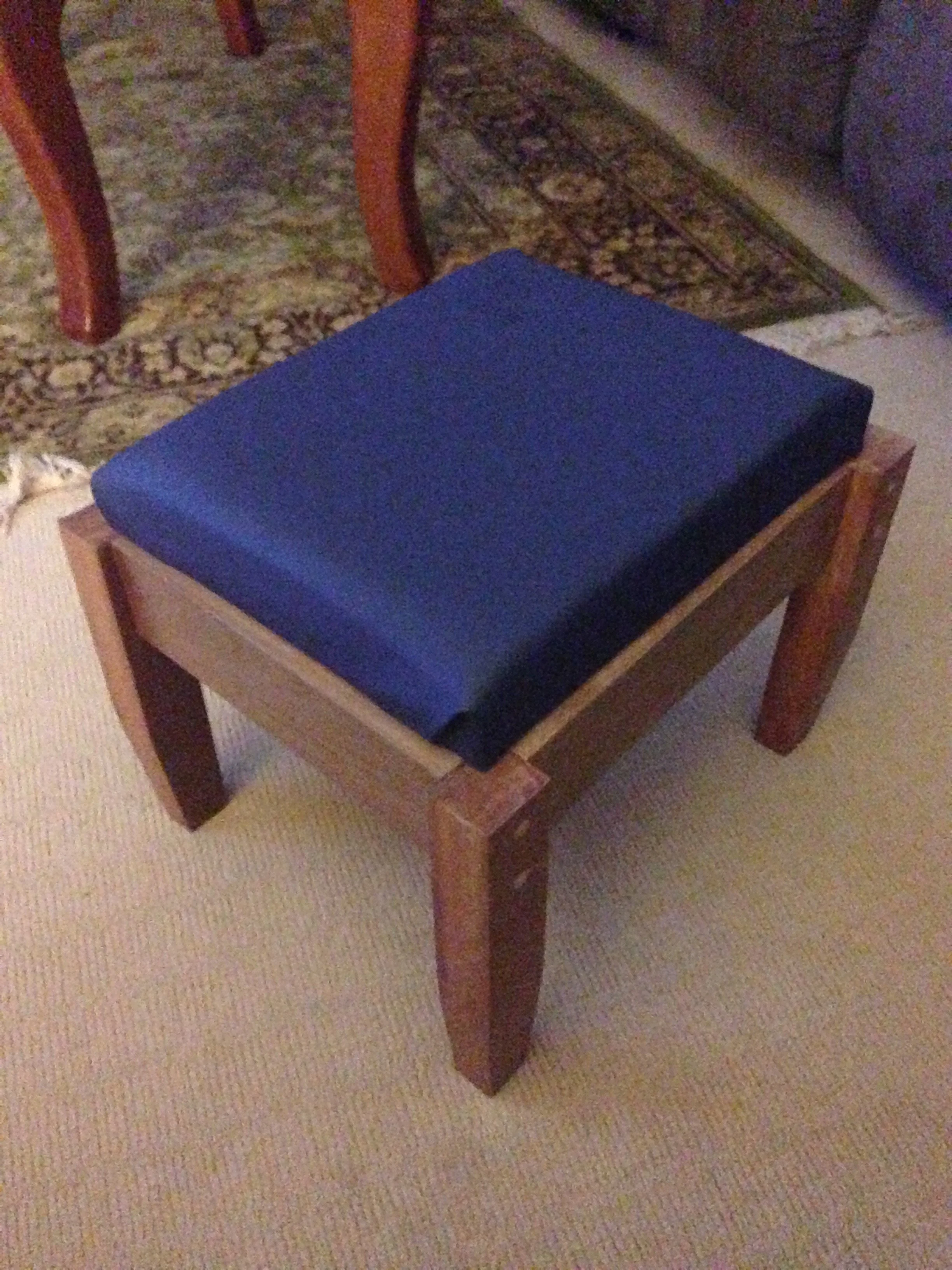 A wooden chair with a blue cushioned seat on a beige carpeted floor.