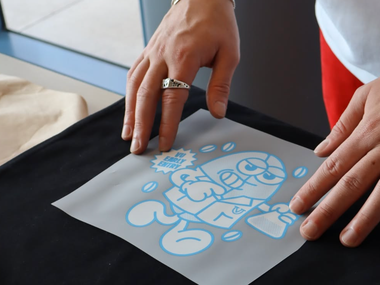 Person applying a blue sticker with cartoon character design and the phrase 'In Every Entry' onto a surface.