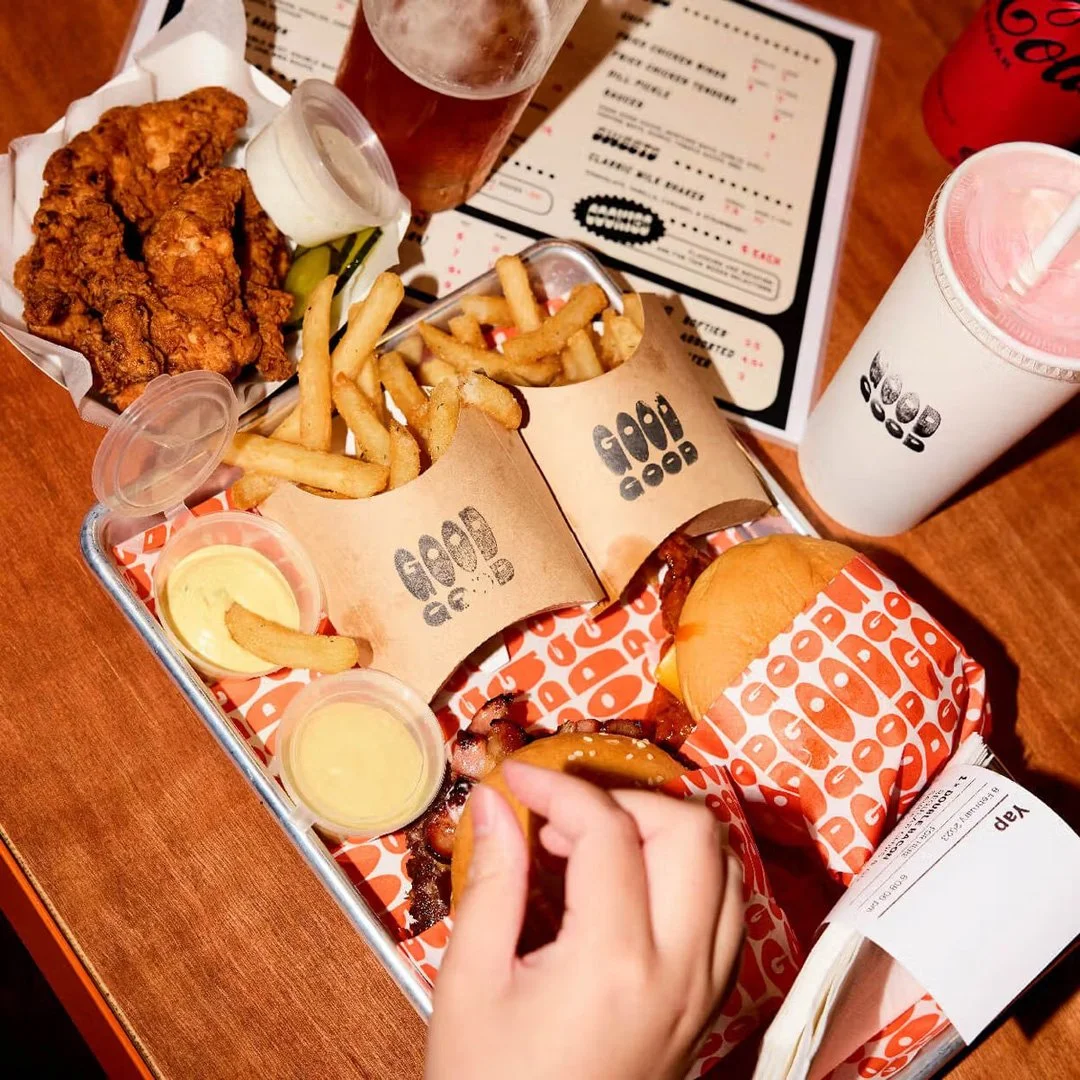 A meal tray with fried chicken, French fries, a burger, sauces, a soft drink, a glass of beer, and a milkshake on a wooden table.