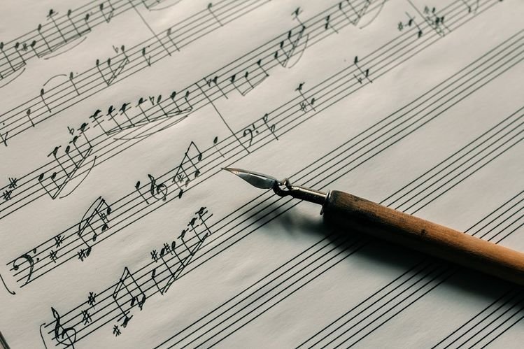 Handwritten musical notes on sheet music with a fountain pen resting on the paper.