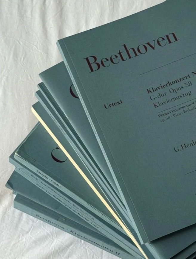 A stack of sheet music books for Beethoven's compositions, with a focus on a book titled 'Beethoven' on a white surface.
