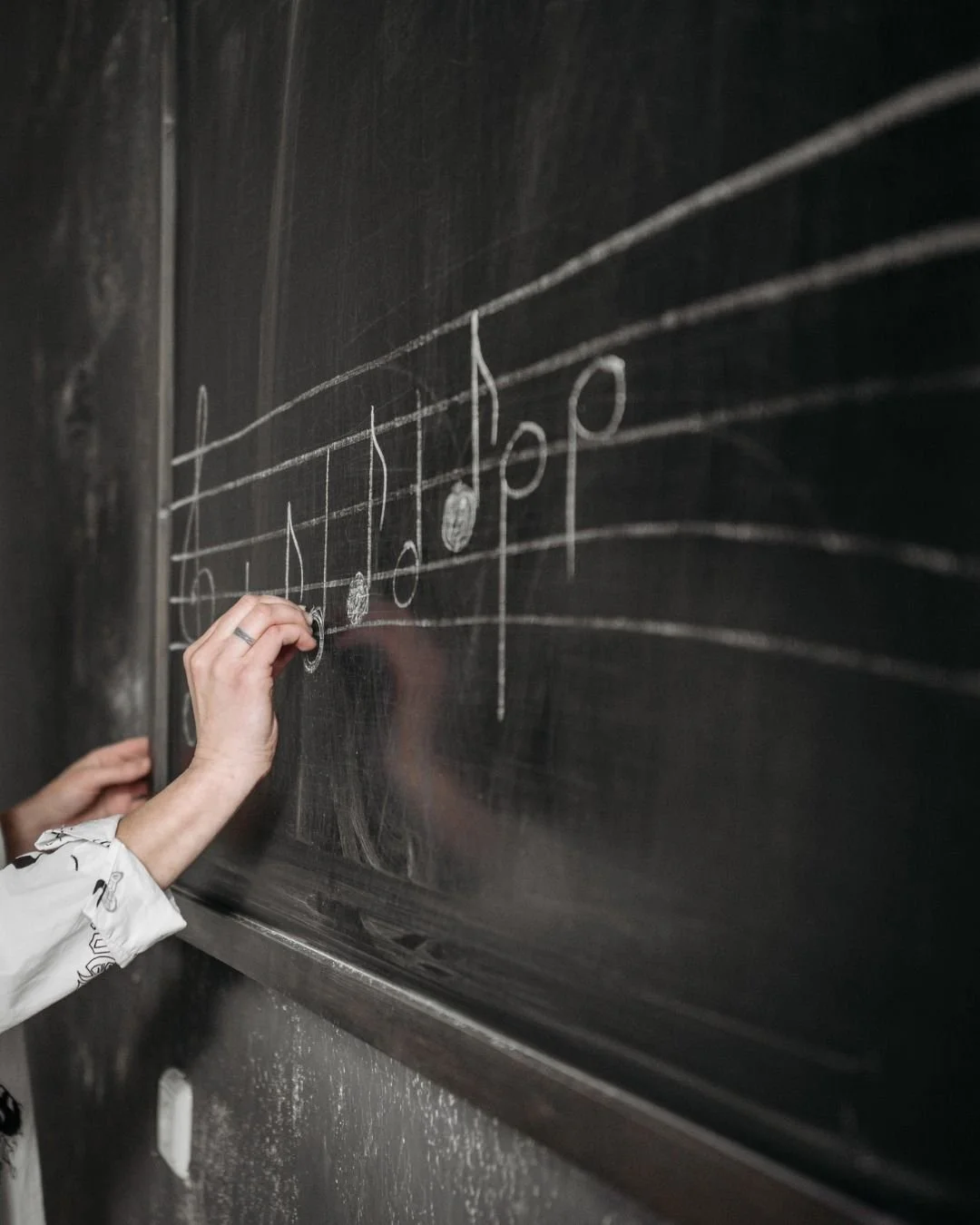 Person drawing musical notes on a black chalkboard.