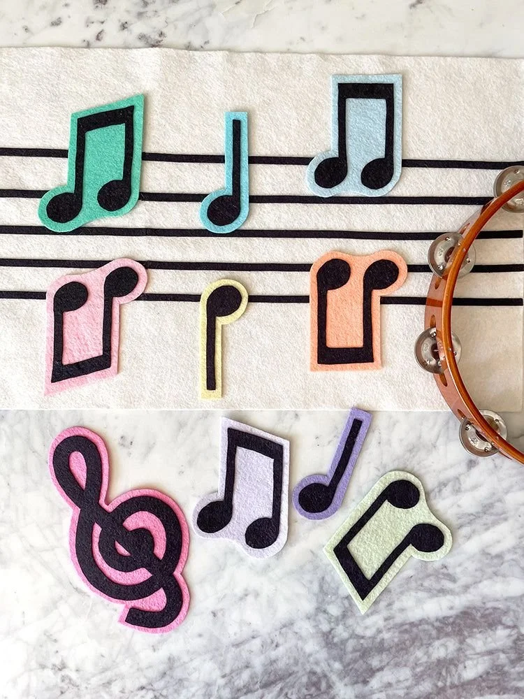 Colorful felt musical notes and a treble clef cutouts on a marble and paper background.
