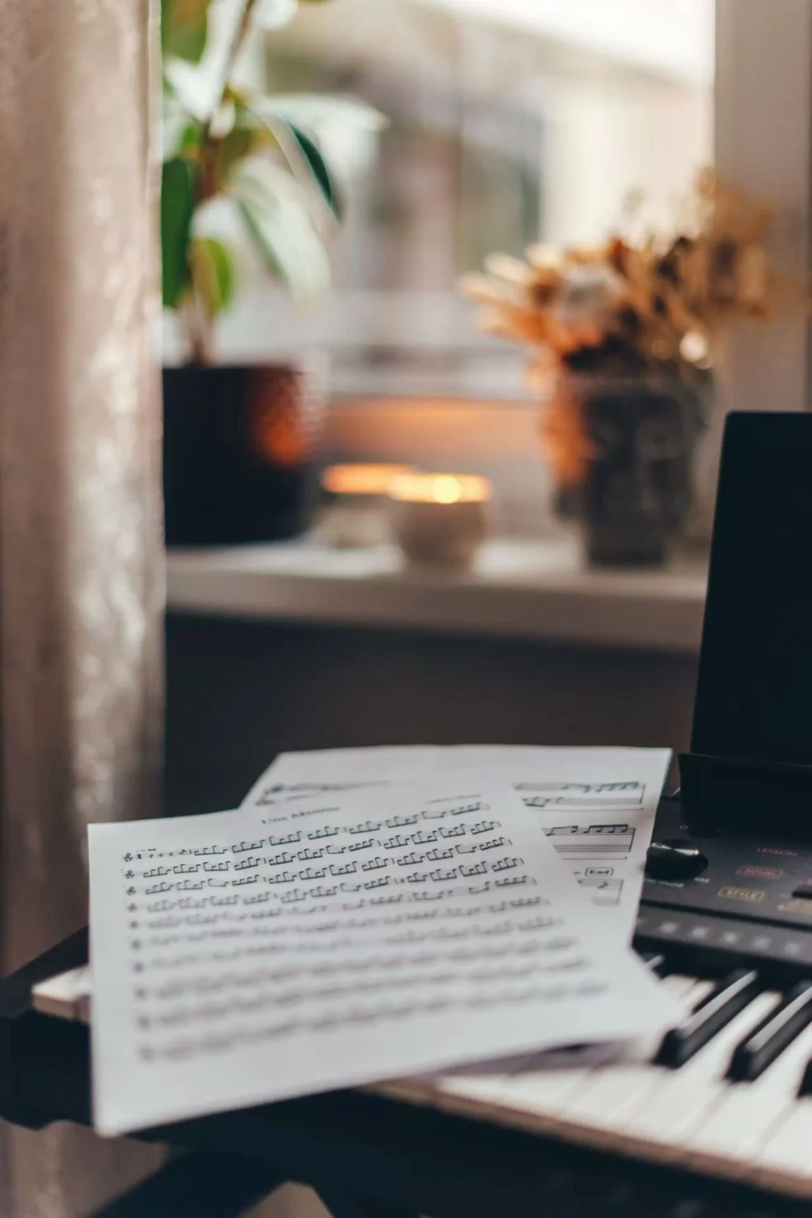 Sheet music on a black piano with sheet music notes, a laptop, and a pen, in a cozy room with a window, plants, and decorative items.