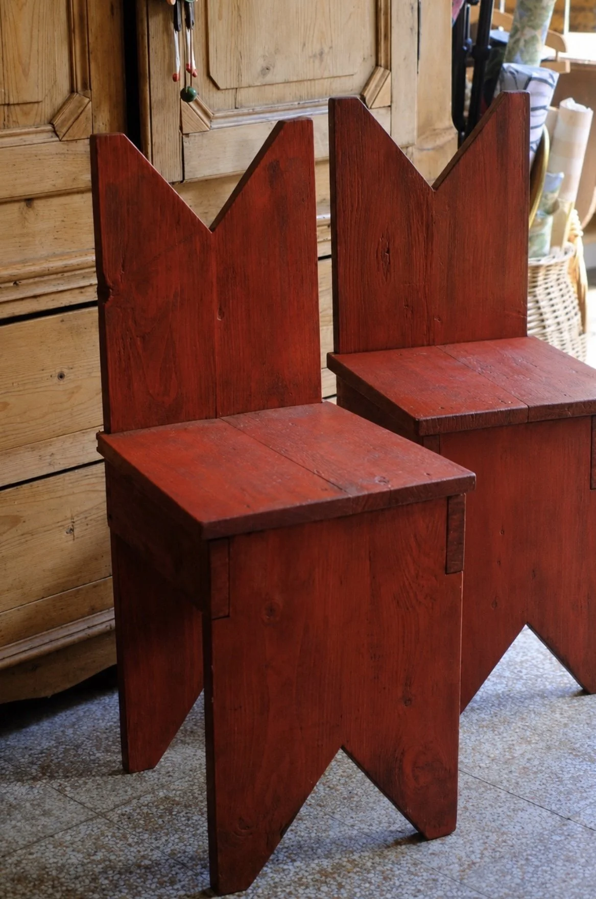 Two wooden chairs with backrests shaped like mountains painted red, set against a wooden cabinet.