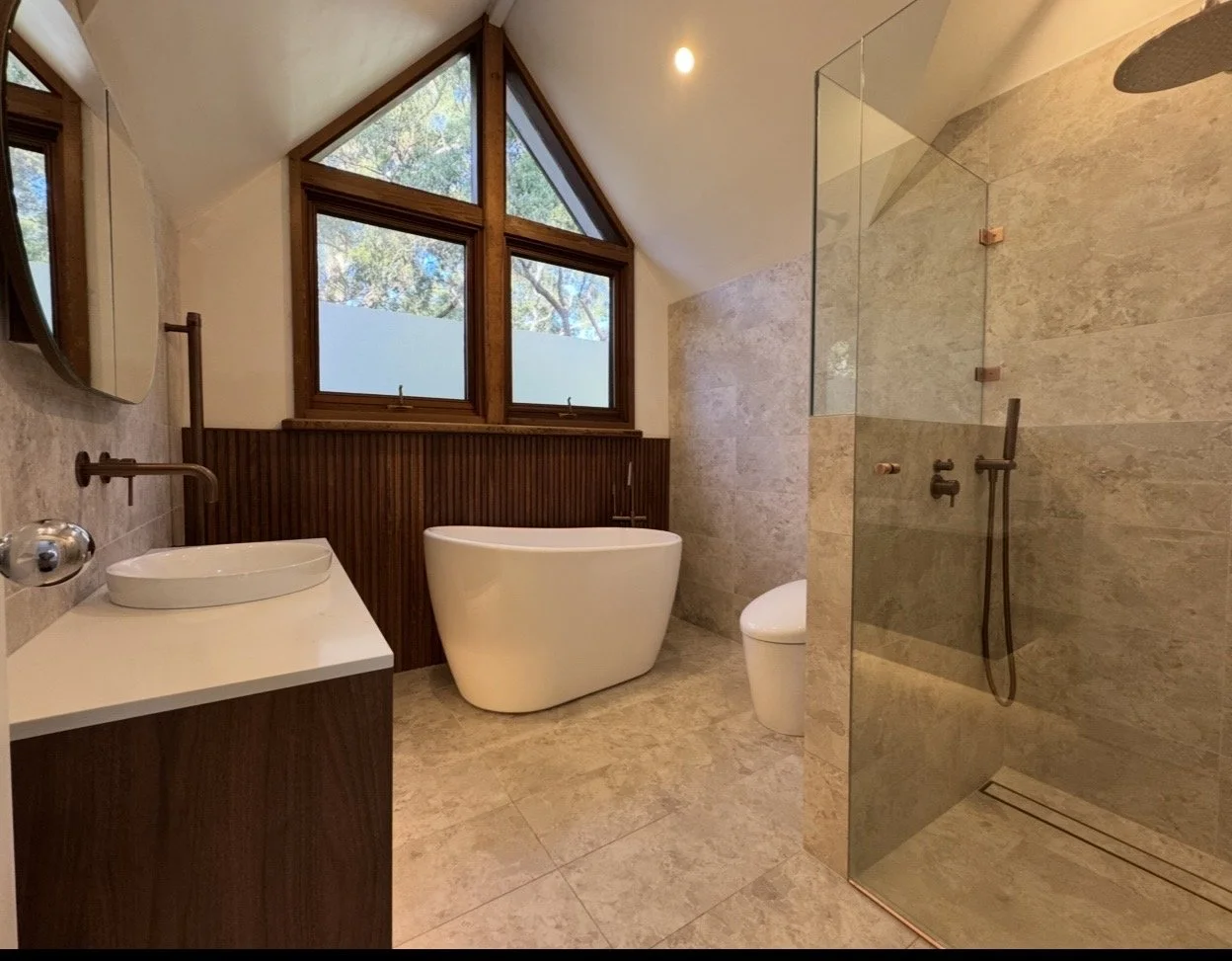 Modern bathroom with large triangular window, freestanding bathtub, walk-in shower with glass door, toilet, and wooden accents.