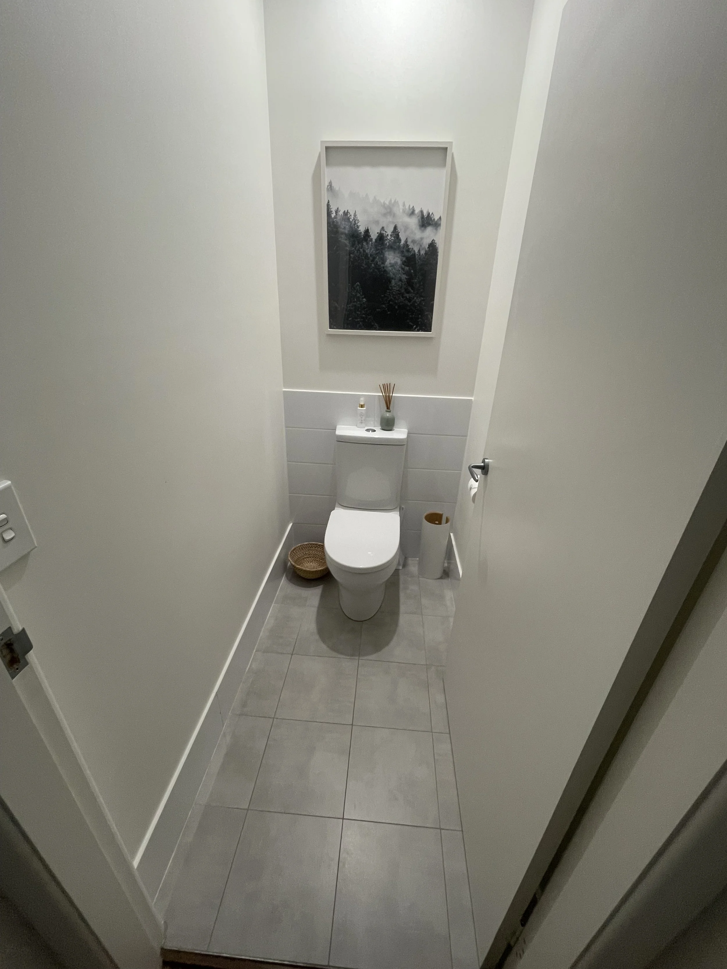 Small modern bathroom with white walls, a framed landscape photo above the toilet, and minimal decor.