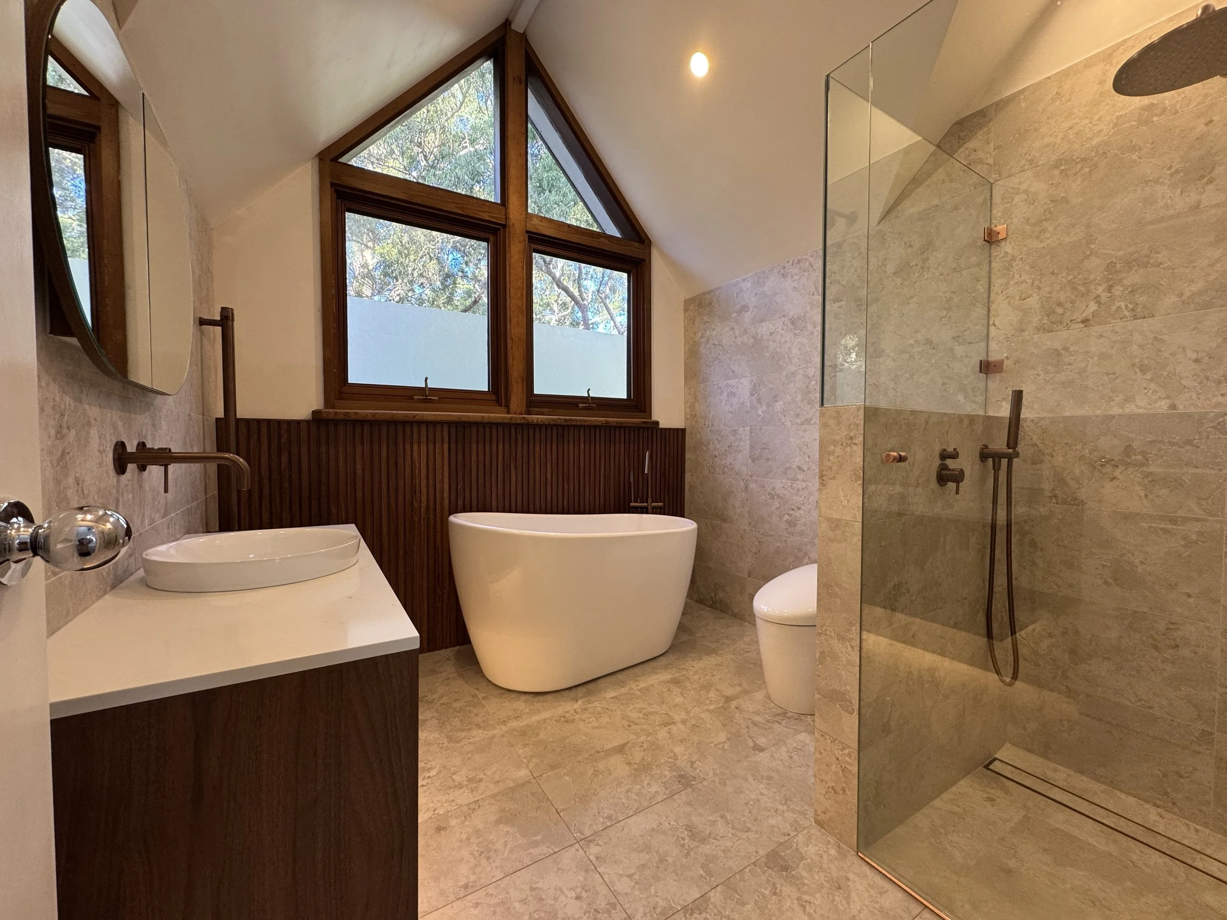 Modern bathroom with large window, freestanding bathtub, wooden accents, and walk-in shower with glass door.