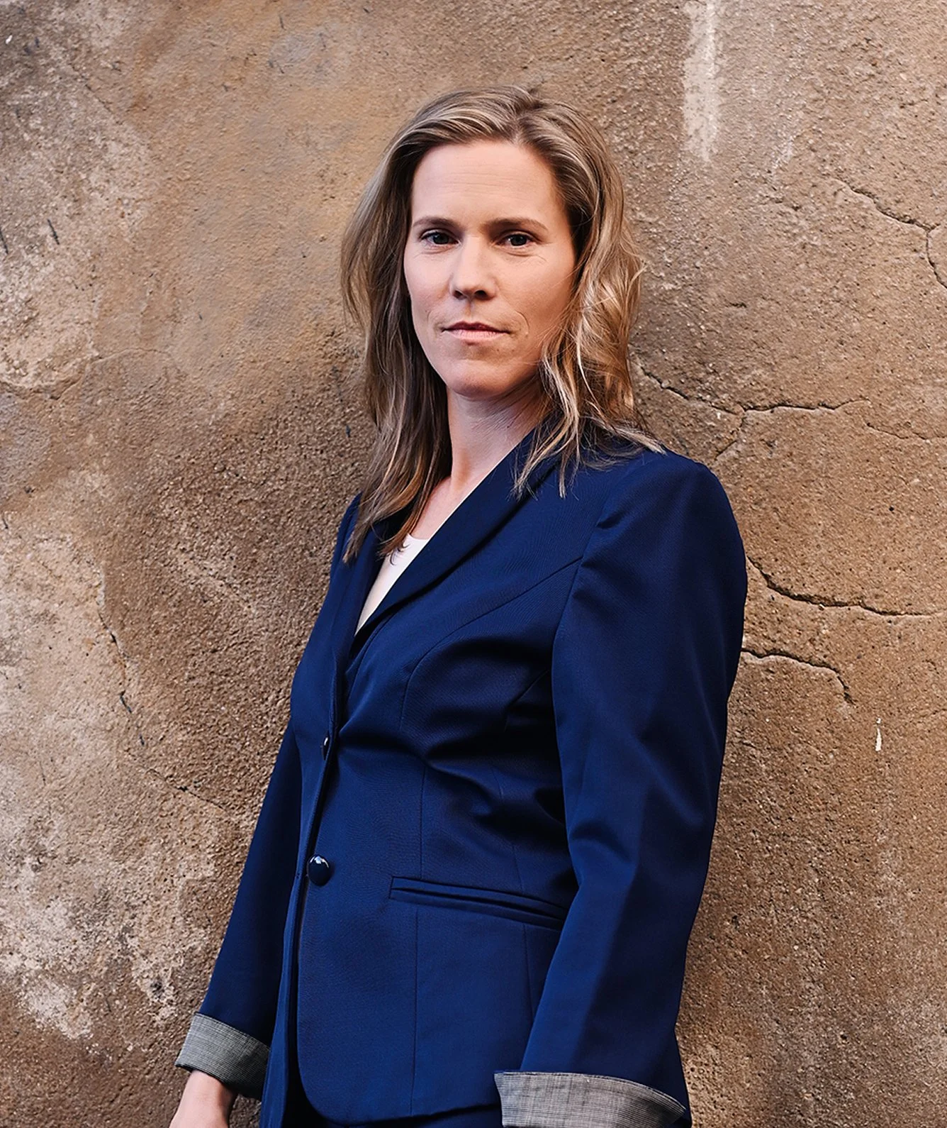 Eine Frau in blauer Blazer steht vor einer bräunlichen Wand.