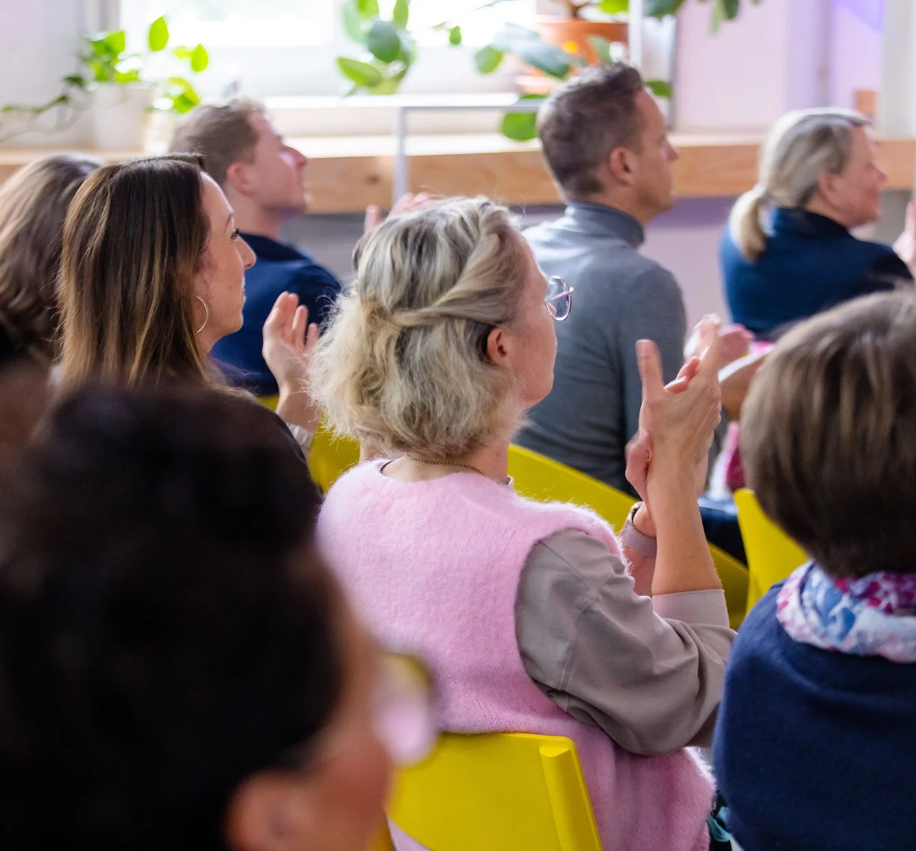Menschen sitzen in einem Raum, klatschen und schauen aufmerksam nach vorne, möglicherweise bei einer Veranstaltung oder Präsentation.