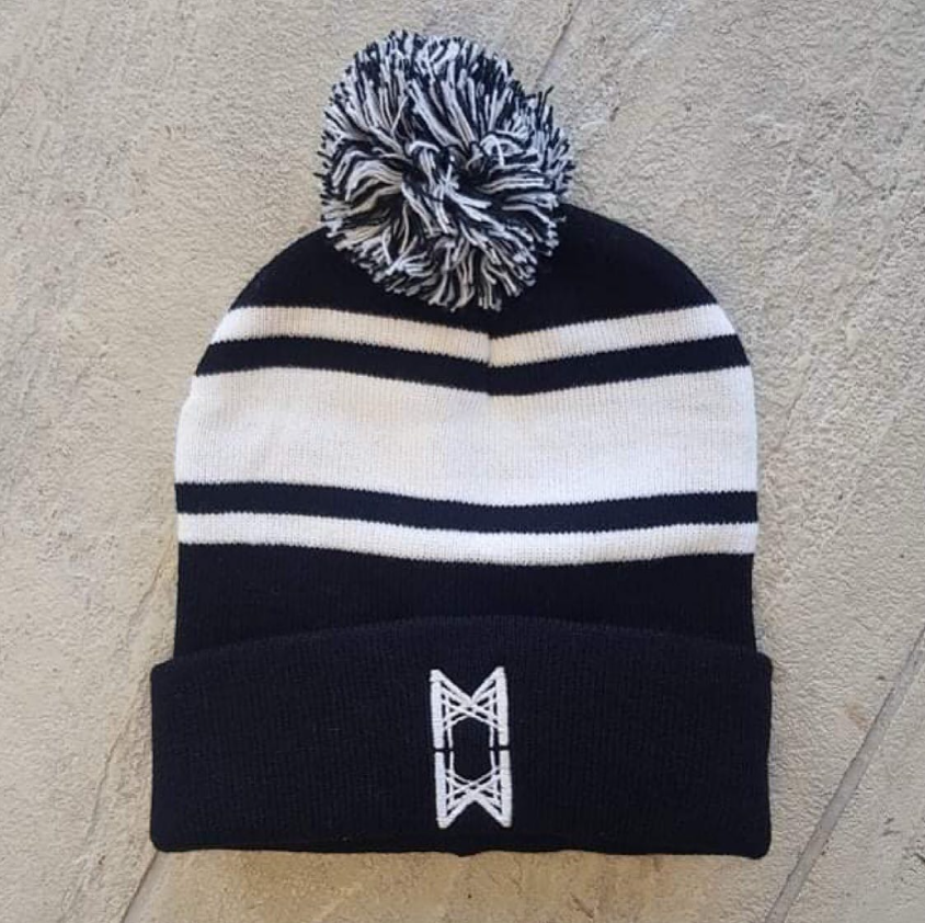 Black and white striped knit beanie hat with a pom-pom on top and a decorative logo on the front.
