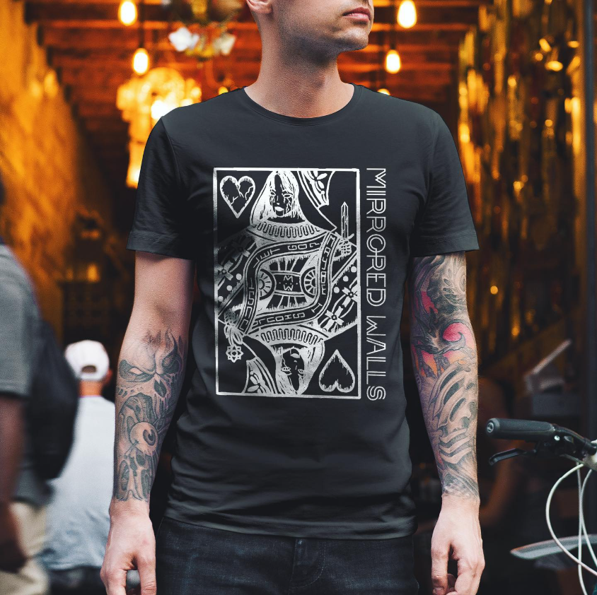 Black T-shirt featuring a white stylized design resembling a playing card with a queen of hearts, and the words 'Mirrored Walls' on the right side. The person has tattoos on both arms and is in a setting with warm lighting.