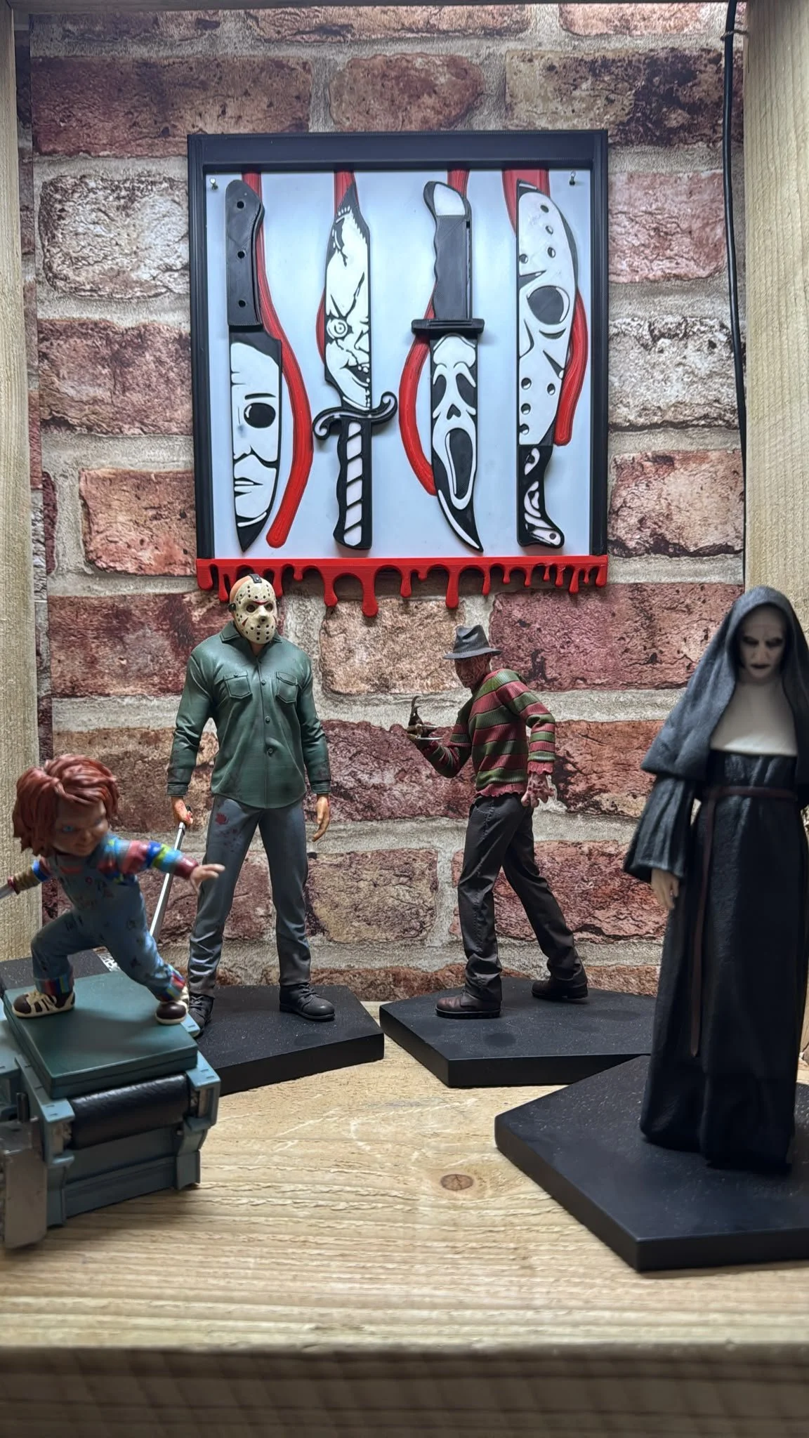 Display of figurines from horror movies including Jason Voorhees, Freddy Krueger, Michael Myers, and Ghostface, arranged against a brick wall background with a graphic design of various knives.