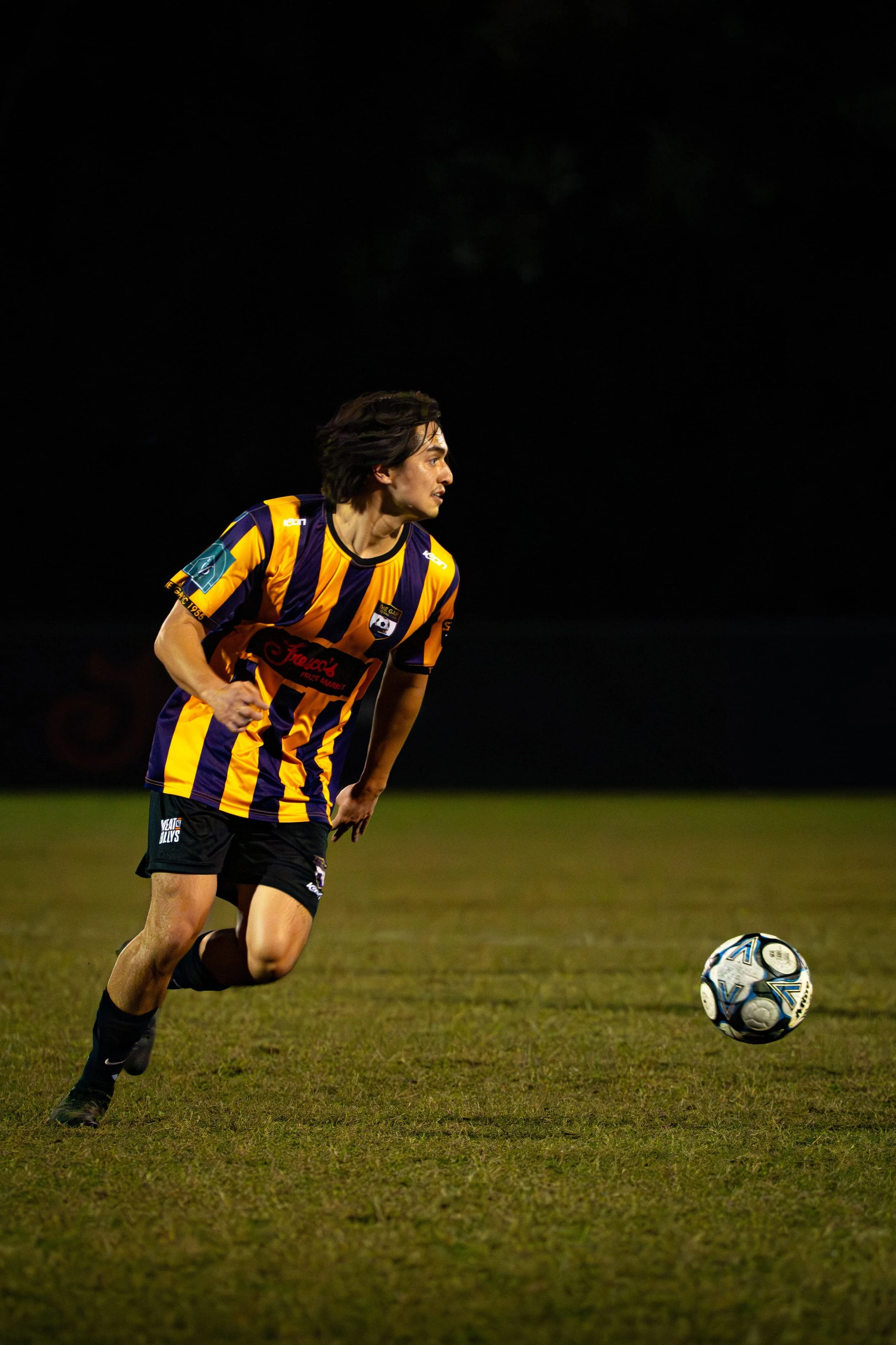 A football player dribbling the ball during a night match at The Gap Football Club.