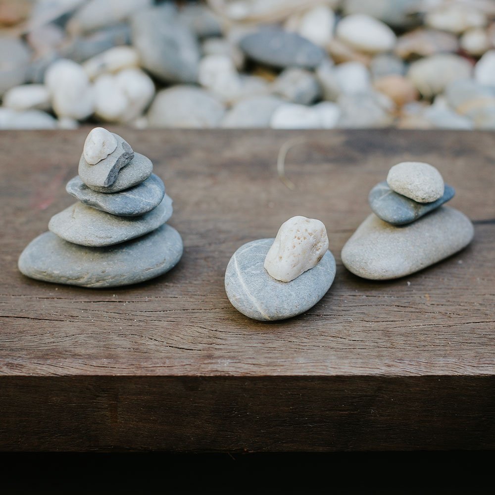 Three small rock stacks on a wooden surface with a gravel background.