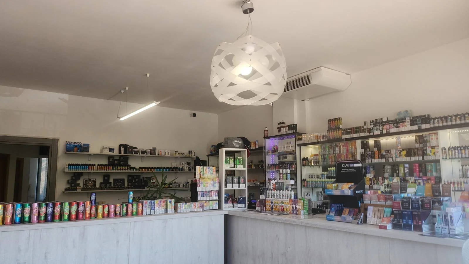 Interno di un negozio con scaffali pieni di prodotti, banconi con articoli in vendita e decorazioni moderne come un lampadario di design e luci rétro.