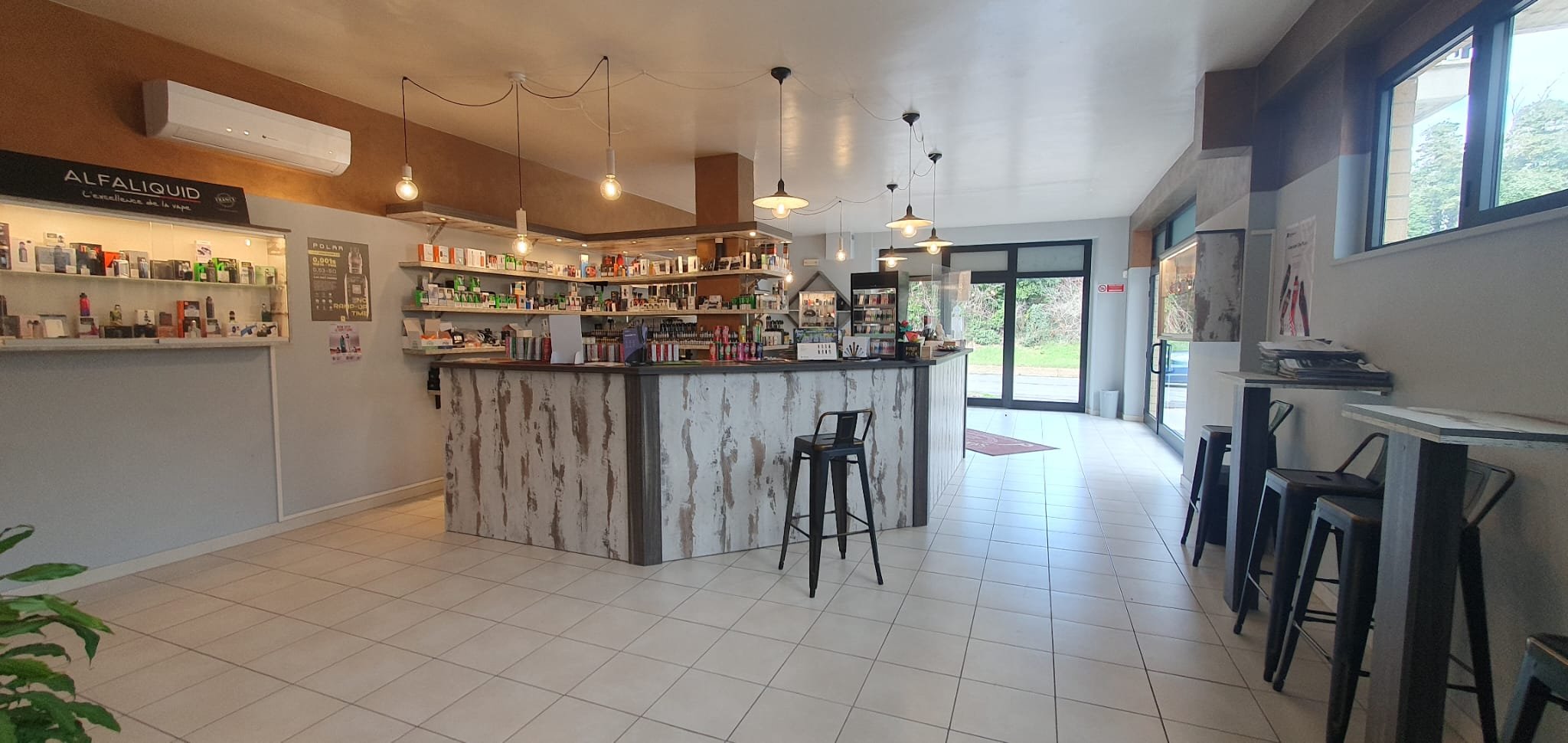 Interno di una caffetteria con bancone centrale, scaffali con prodotti, sedie nere, grandi finestre con vista all'esterno e decorazioni minimaliste.