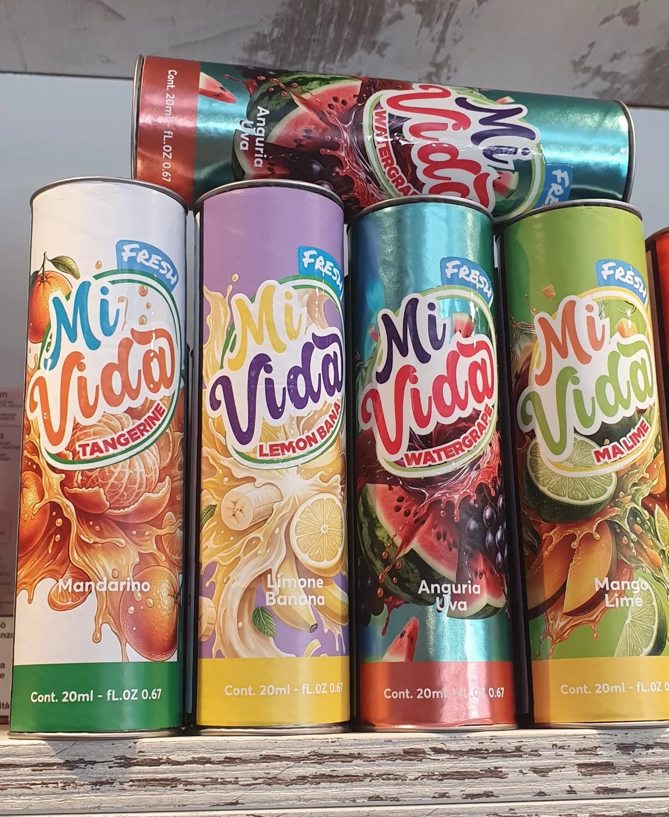 Confezioni di succhi di frutta Mi Vida in diversi gusti: mandarino, limone banana, anguria uva, mango lime. Le confezioni sono cilindriche con etichette colorate e immagini di frutta.