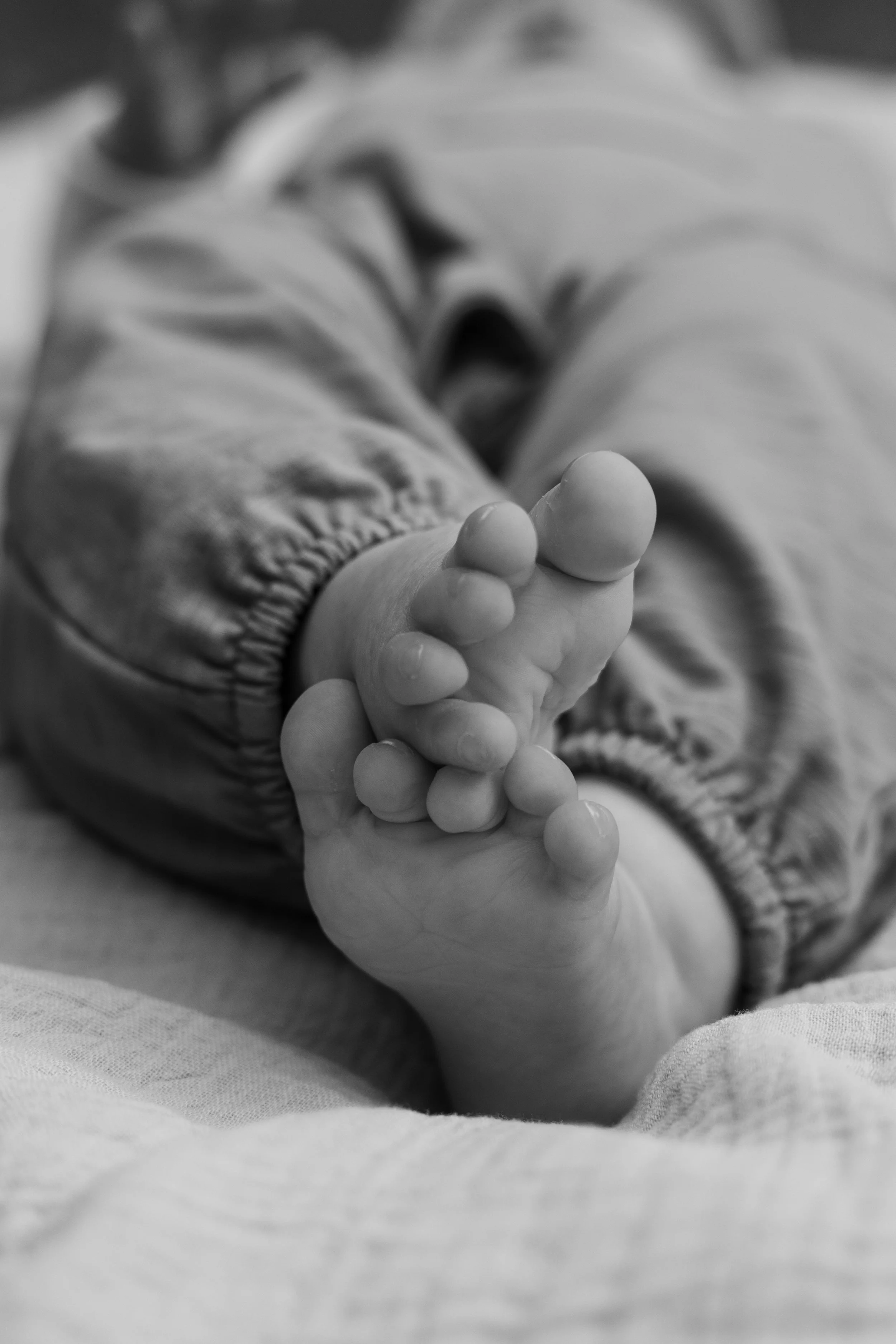 Nahaufnahme einer Kinderhand, die auf einer weichen Oberfläche liegt, im Fokus die kleinen Finger. Das Bild ist in Schwarz-Weiß gehalten.