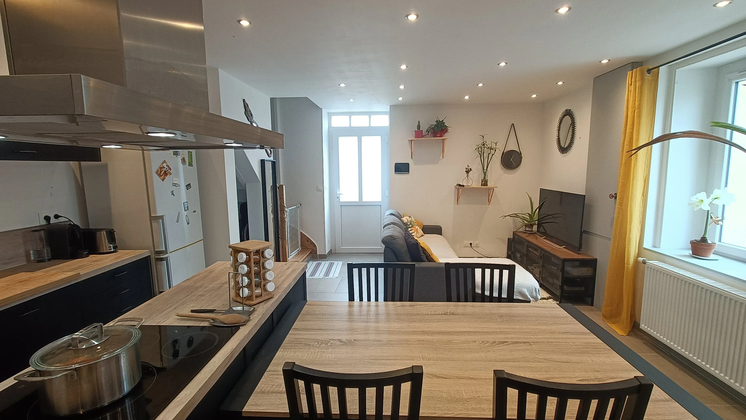 Intérieur d'un salon avec canapé, télévision, étagères décoratives et fenêtres avec rideaux jaunes.