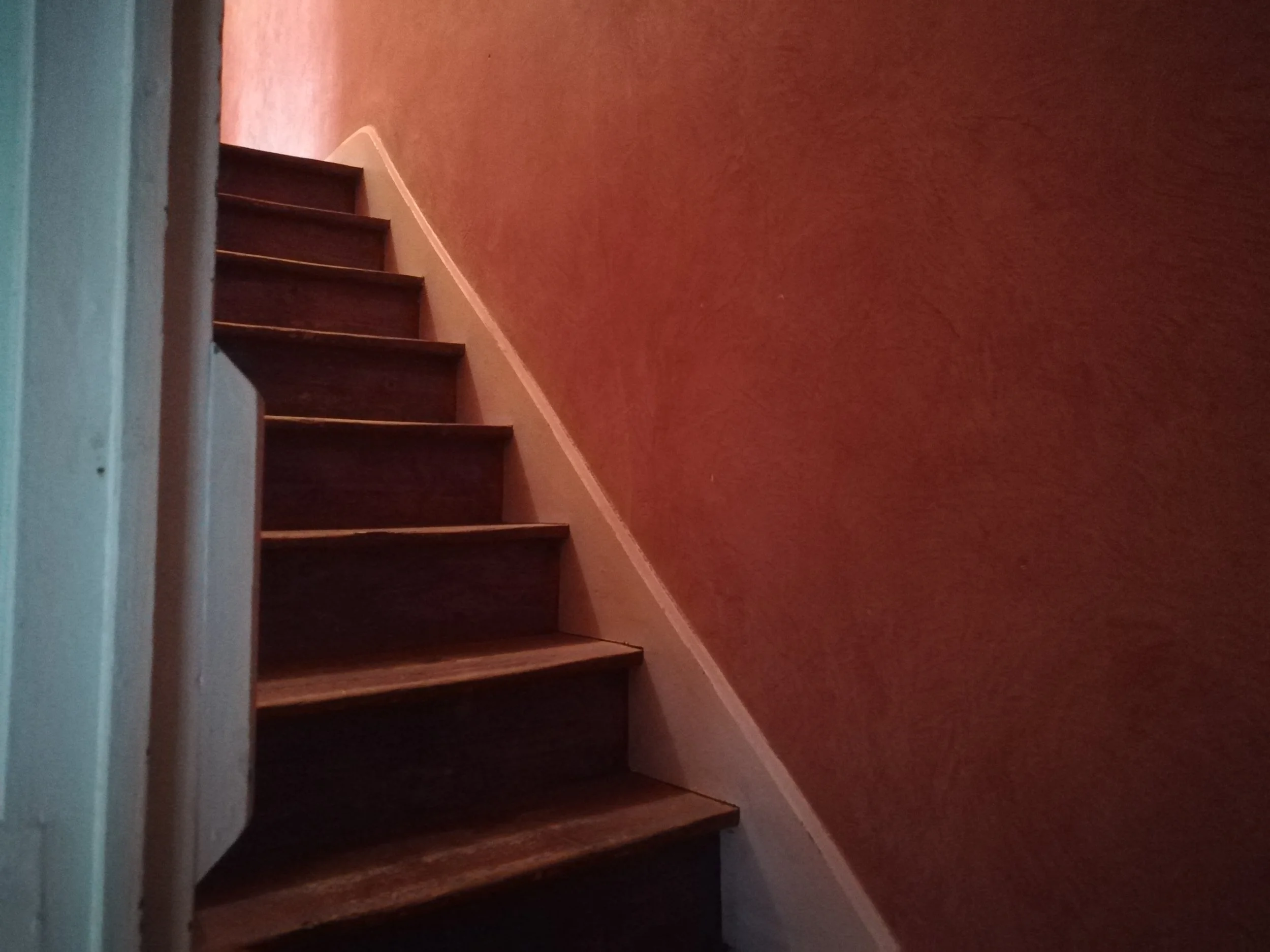 Escalier en bois avec tapis rouge en haut, murs roses dans un intérieur