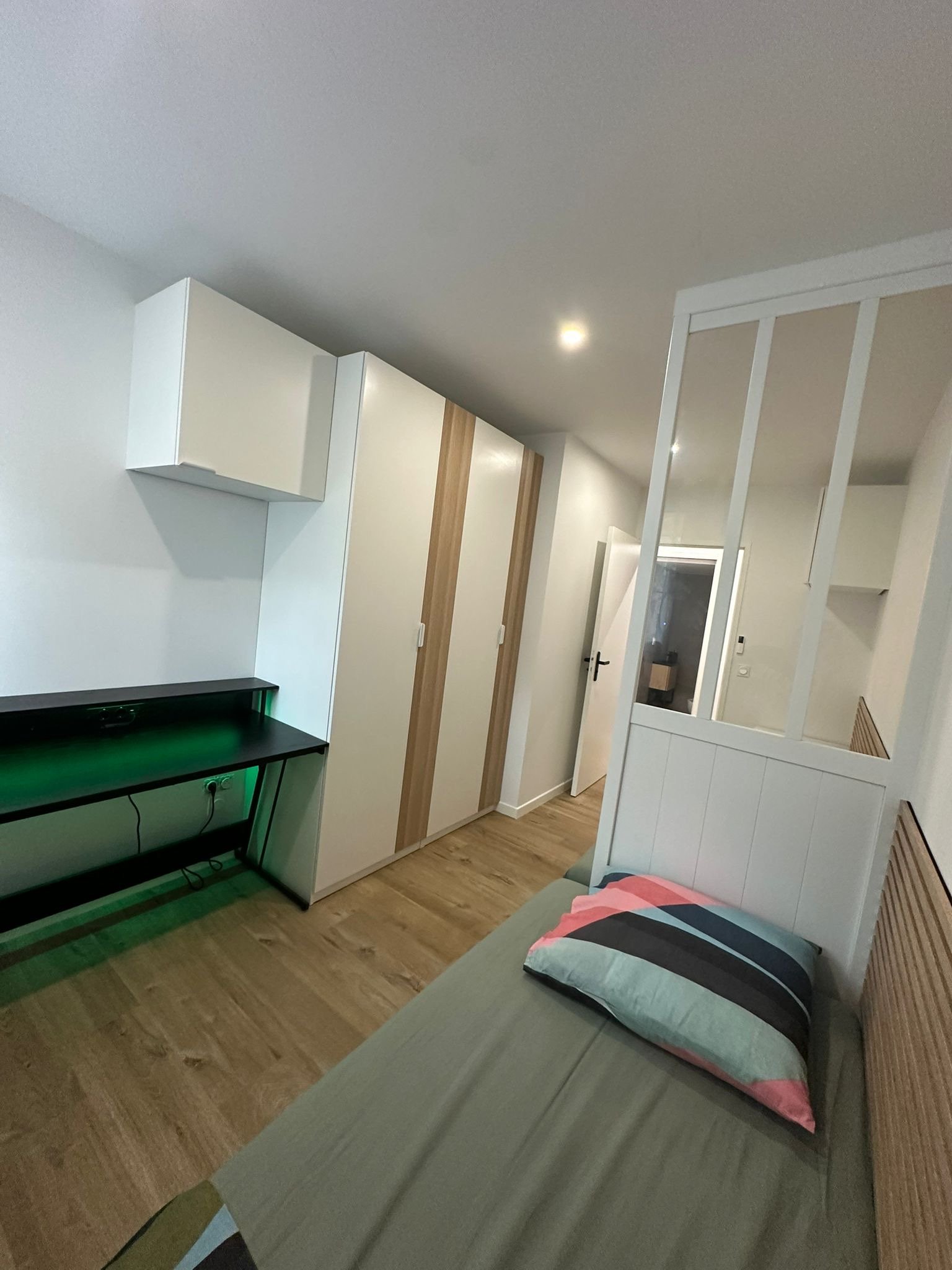 Salon avec canapé gris, oreiller multicolore, meubles blancs, un mur en bois, un mur blanc, sol en parquet, porte et fenêtre, meubles encastrés et meuble TV.