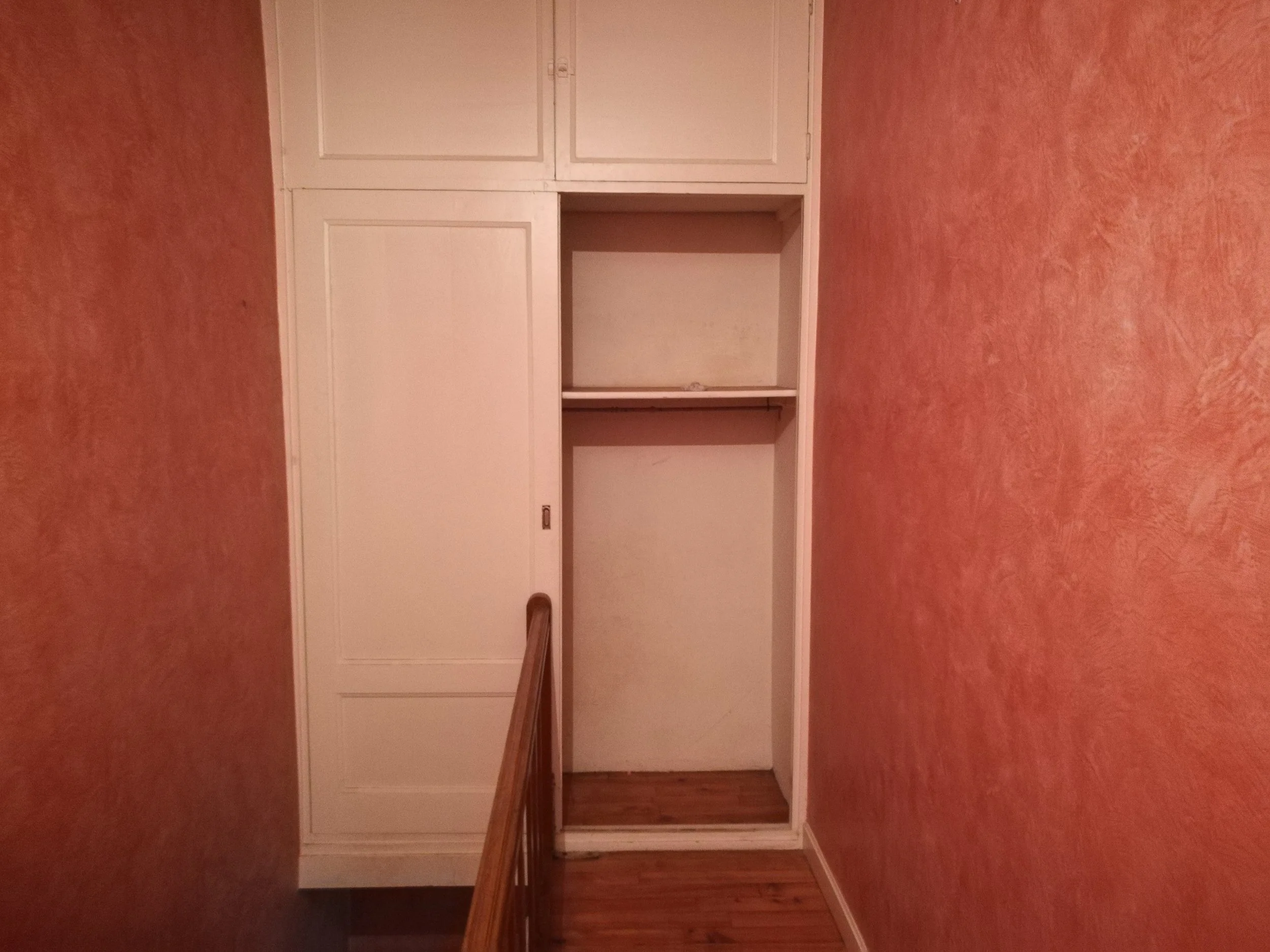 Une grande armoire ou placard blanc sans portes dans une pièce avec un mur orange ou rouge.