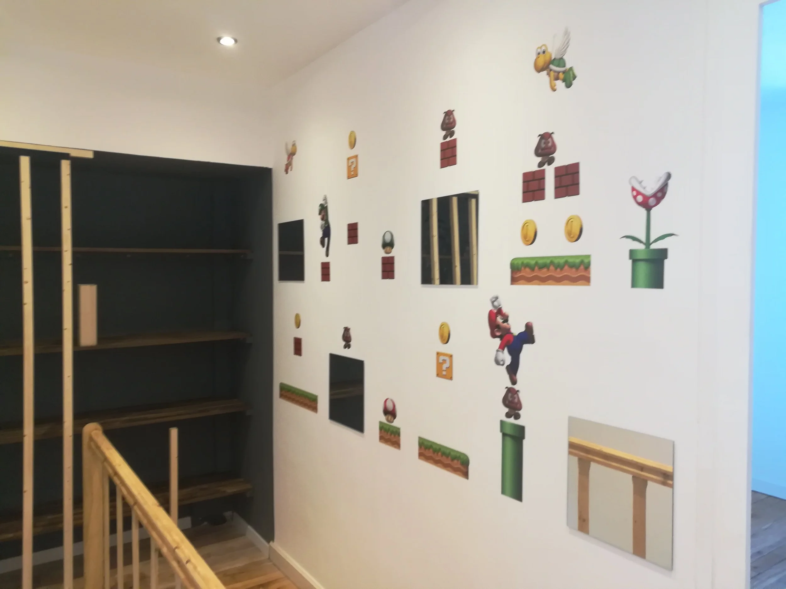 Mur intérieur avec des stickers de jeu vidéo Super Mario, comprenant des pièces d'or, des blocs rouges, des champignons, Luigi et Yoshi, créant une décoration thématique.