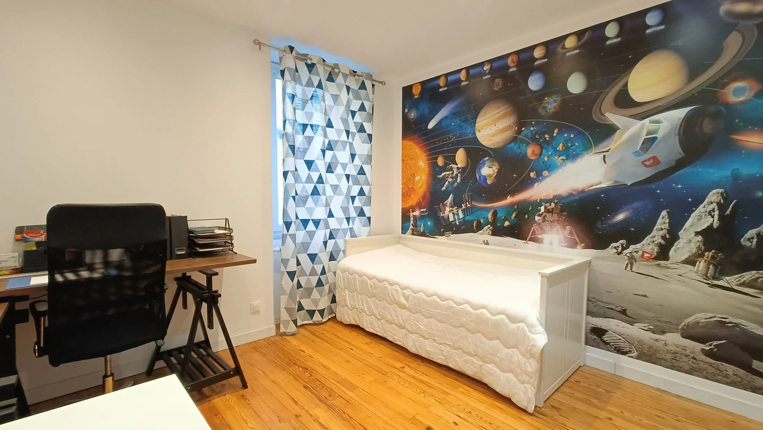 Chambre avec mur à thème espace, affichant des planètes et une station spatiale, ramenant à la surface de la lune ou de Mars.