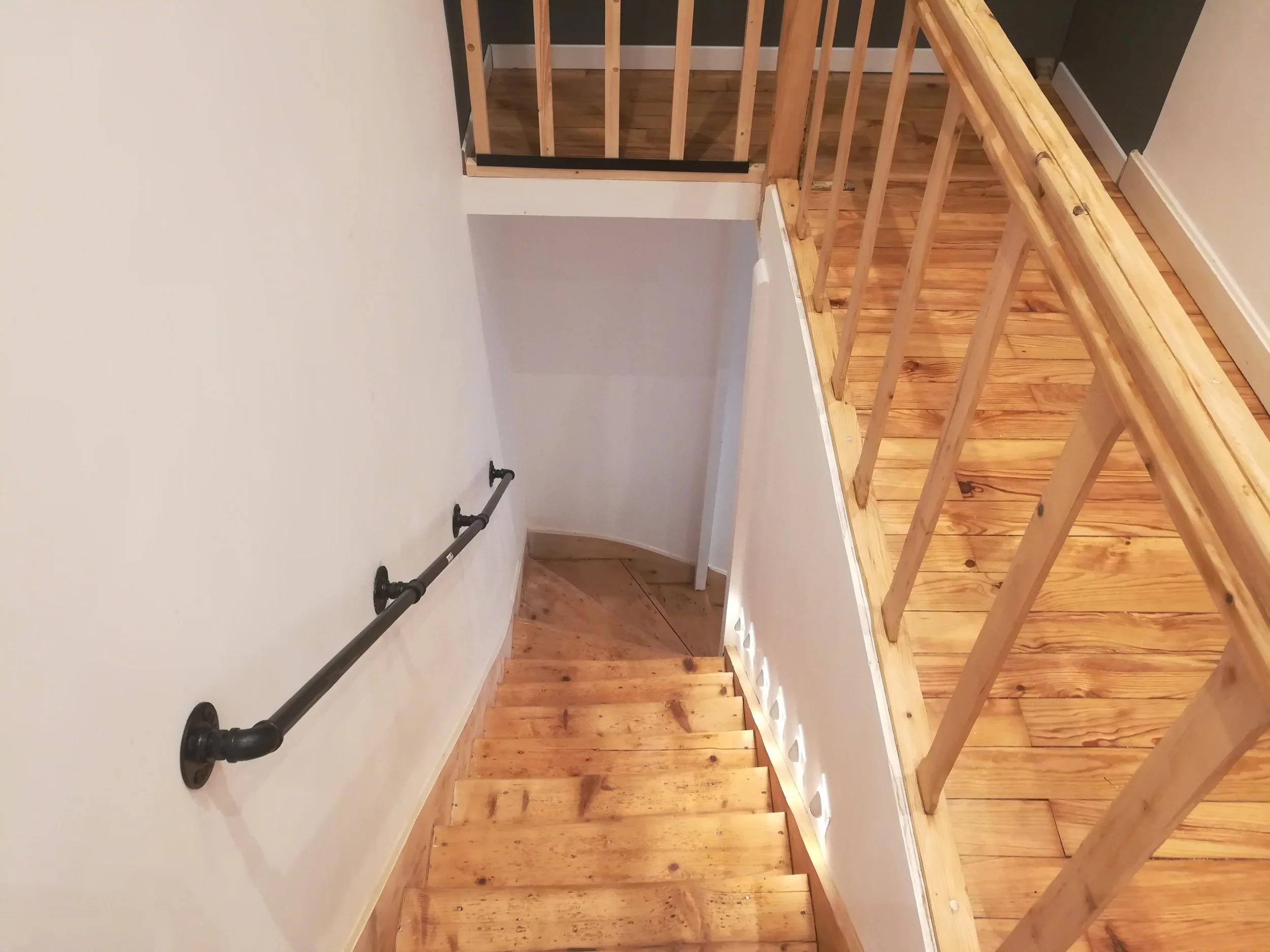 Escalier en bois avec garde-corps en bois, pas encore terminé, dans une pièce avec murs blancs et sol en bois